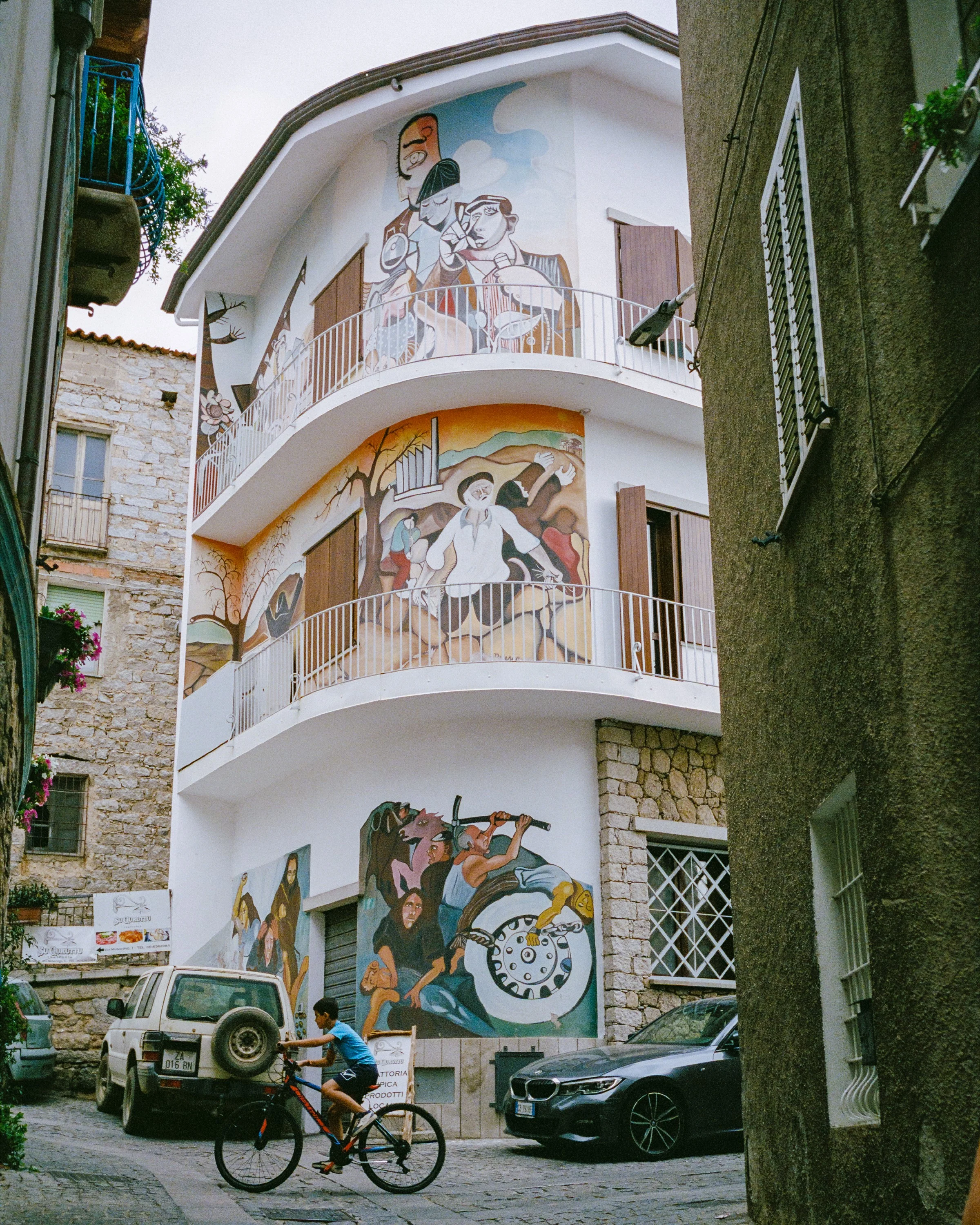 Painted murals covering a house in Orgosolo, a cyclist below