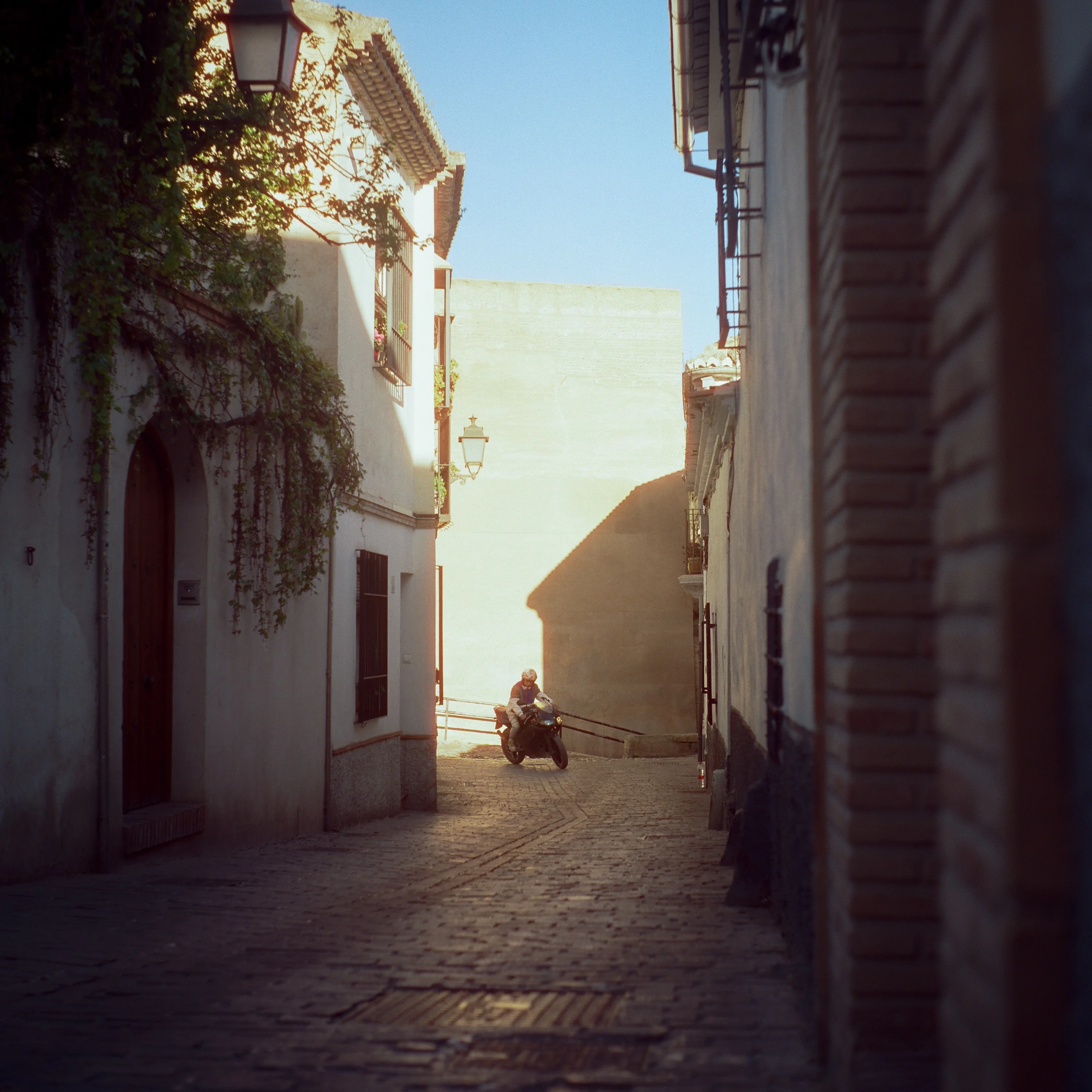 A motorbike in a narrow sunlit lane between tall old houses