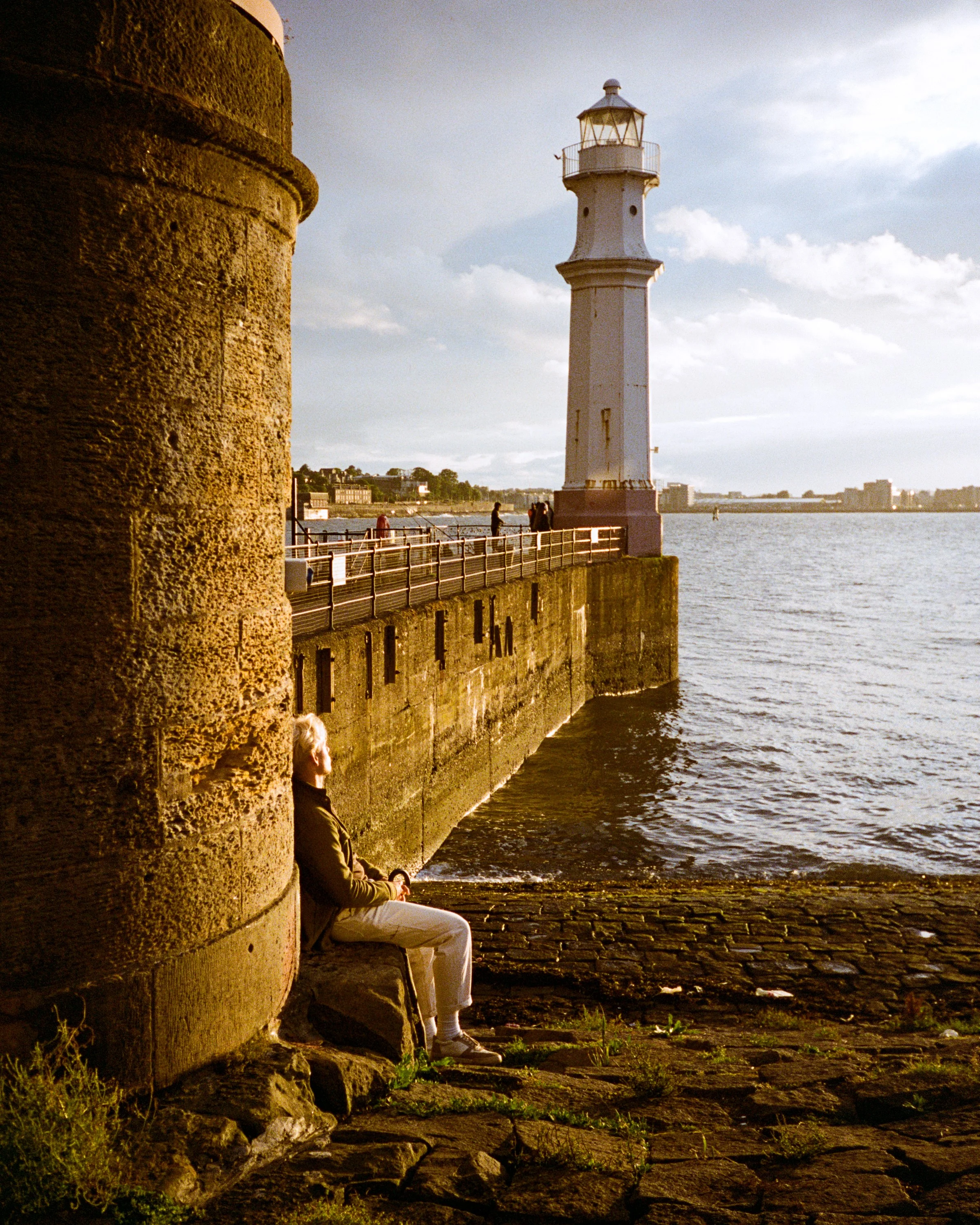 A woman sitting below the harbour wall at Newhaven, the lighthouse behind