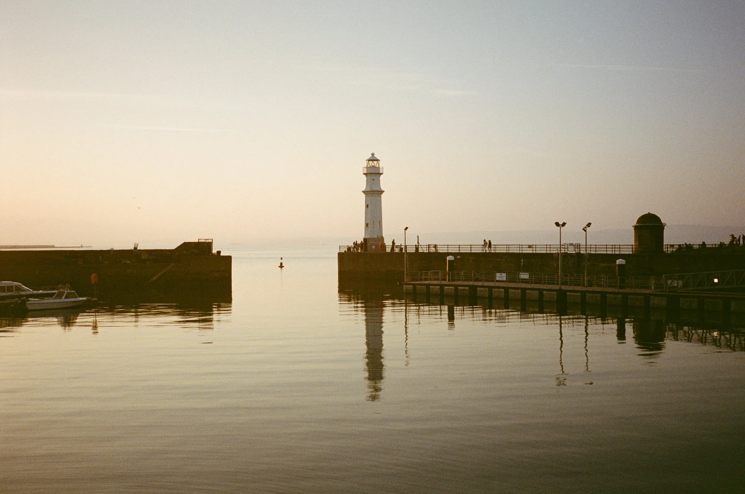 Newhaven lighthouse and harbour wall reflected in flat water at dusk