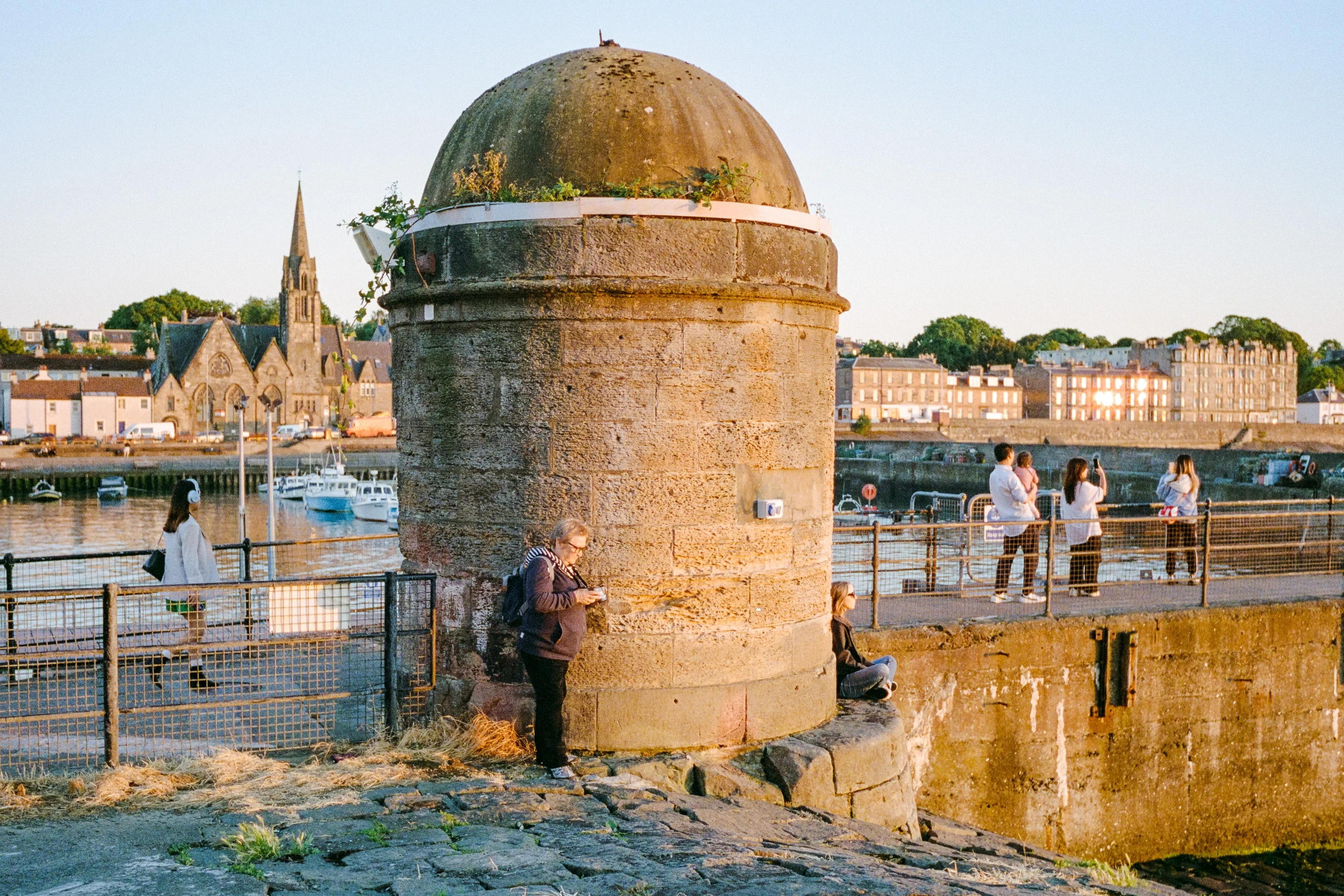 A round stone tower on Newhaven harbour, Leith spires behind