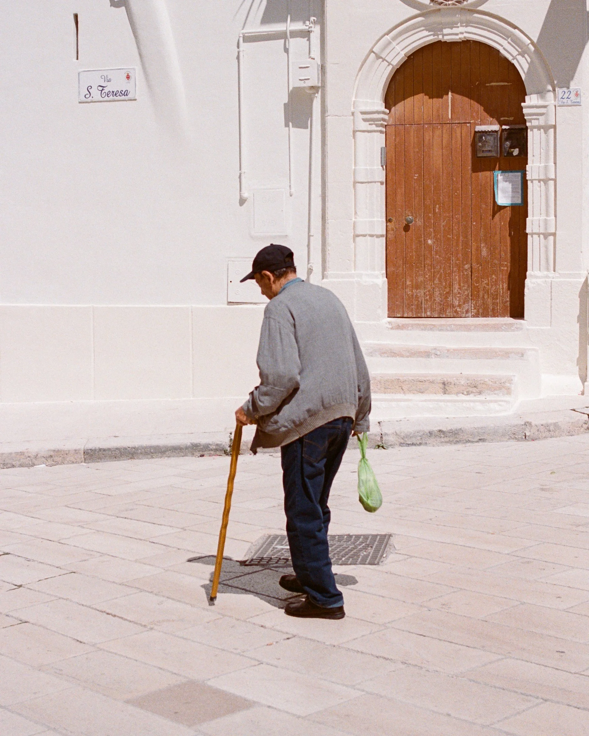 An old man with a cane walks past a white church door