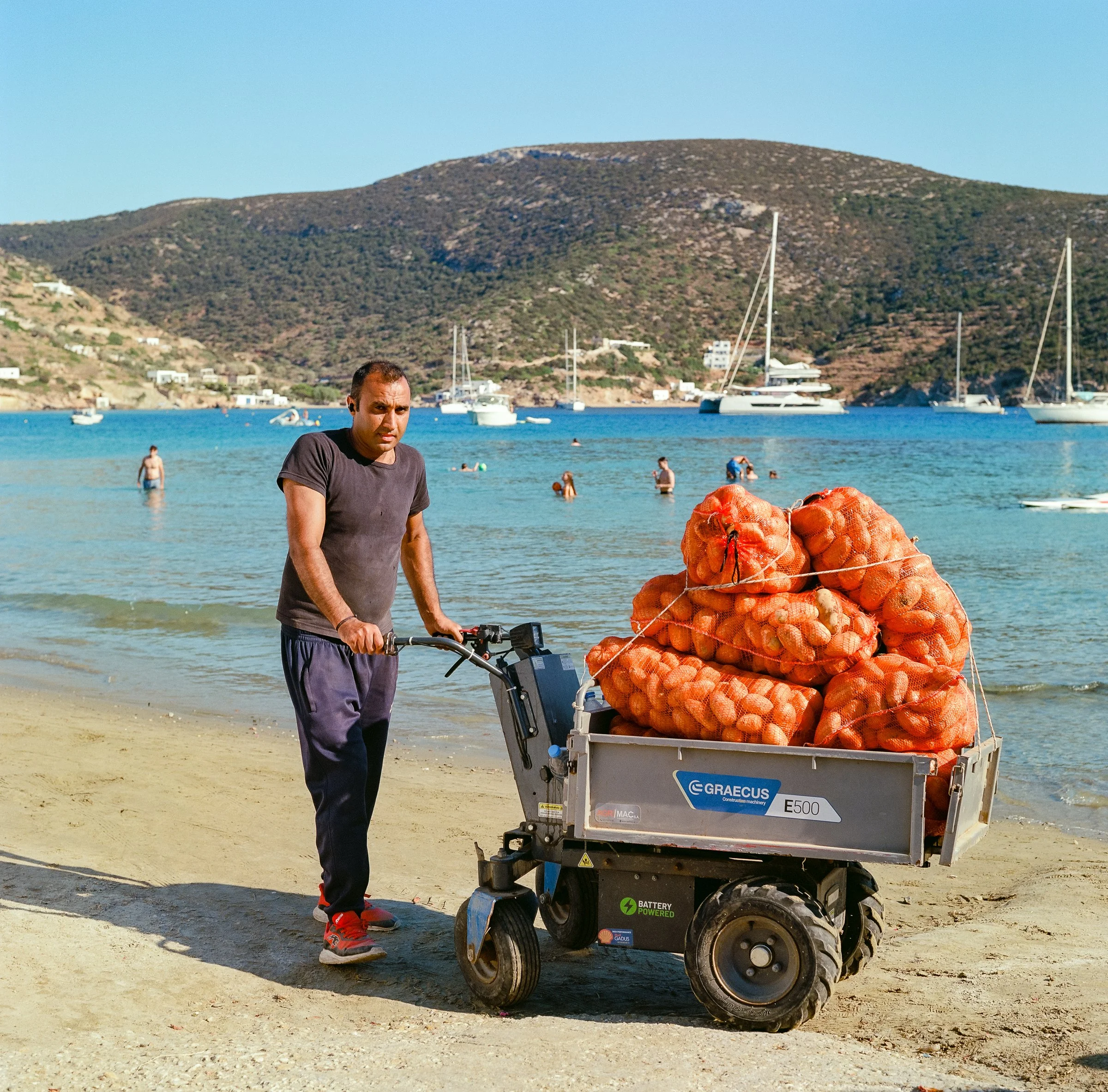 A man pushes a trolley stacked with orange sacks through a white village