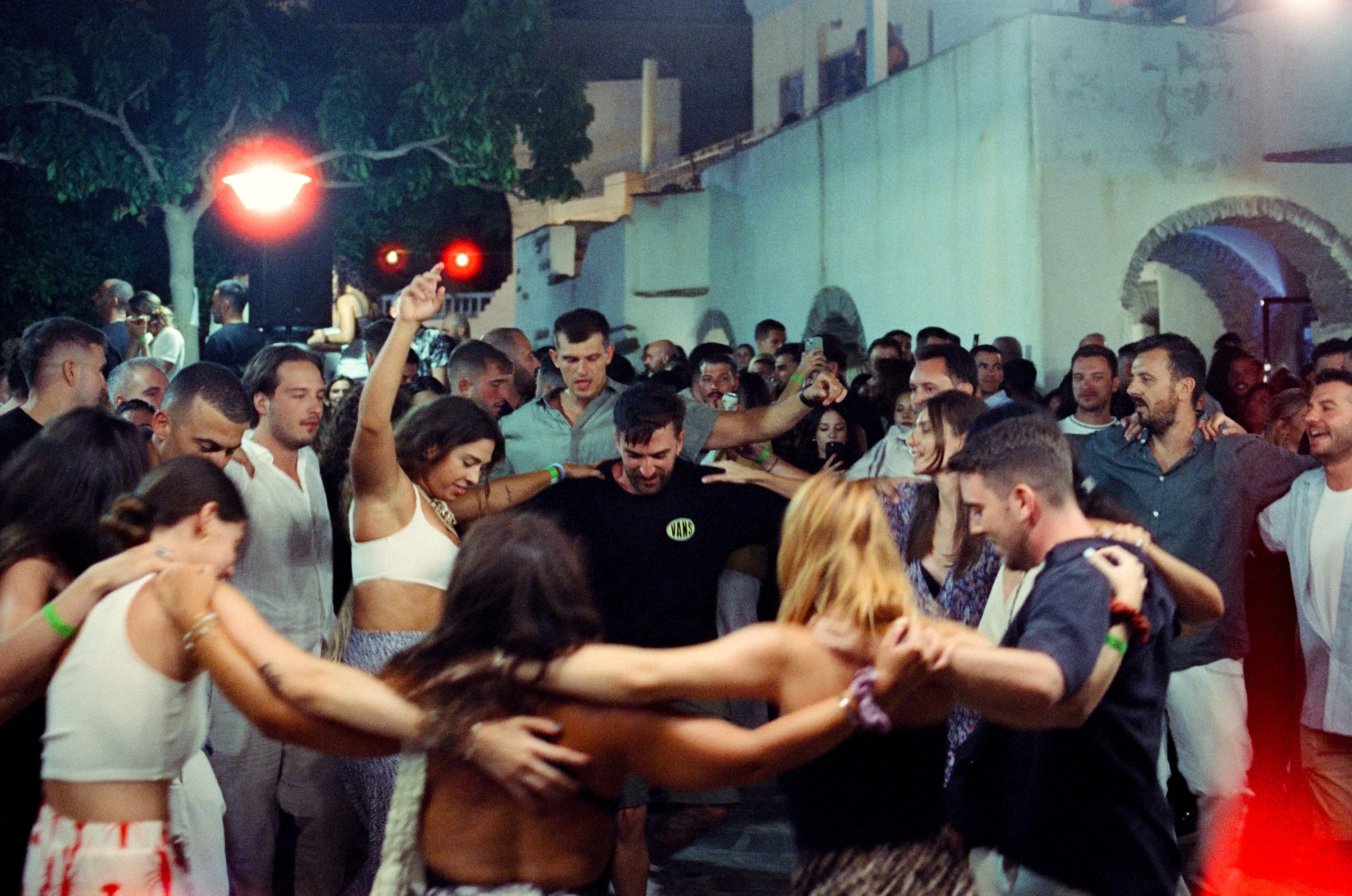 A crowd dancing arm in arm at a night festival in a village square