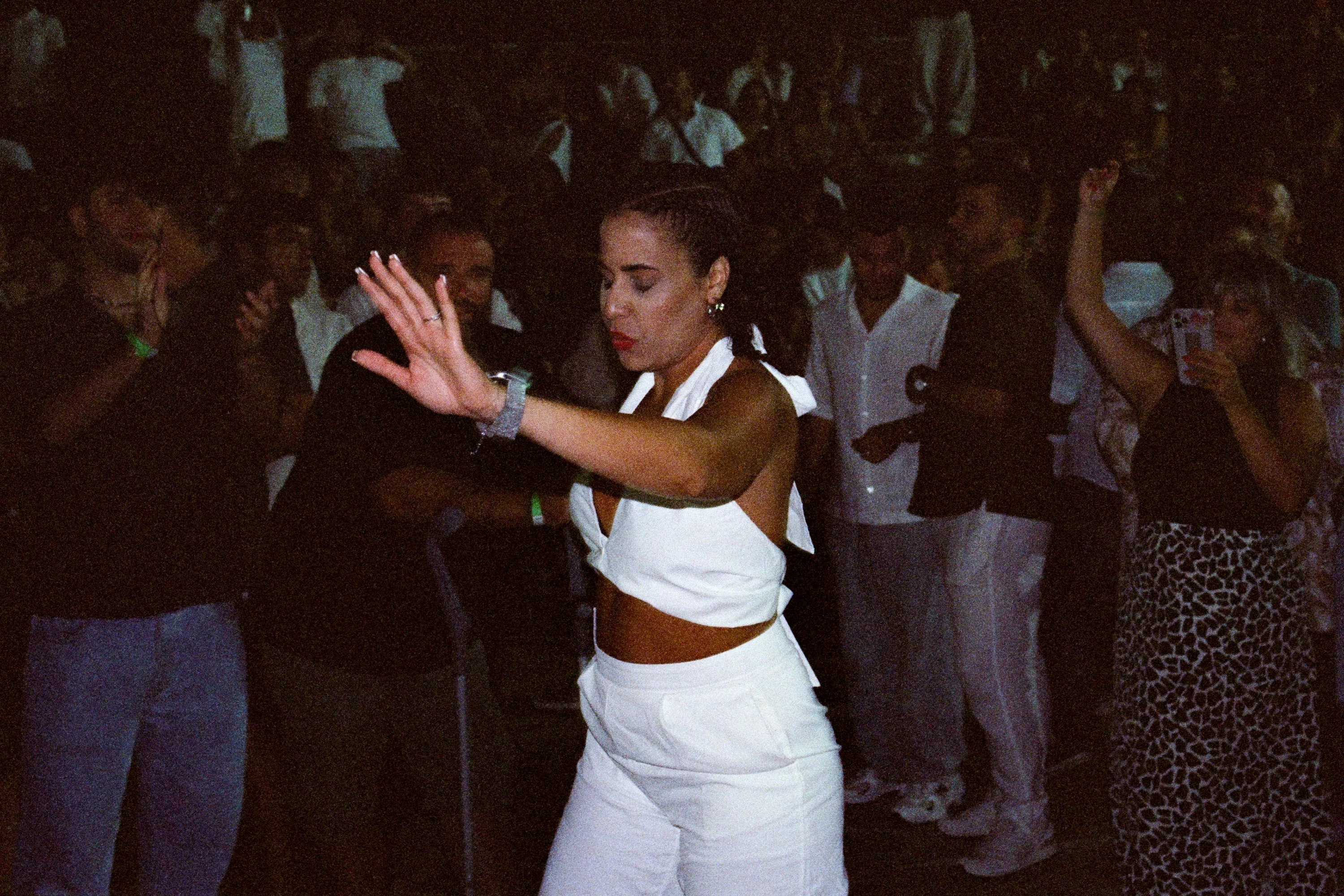 A woman in white dancing with one arm raised at a night festival