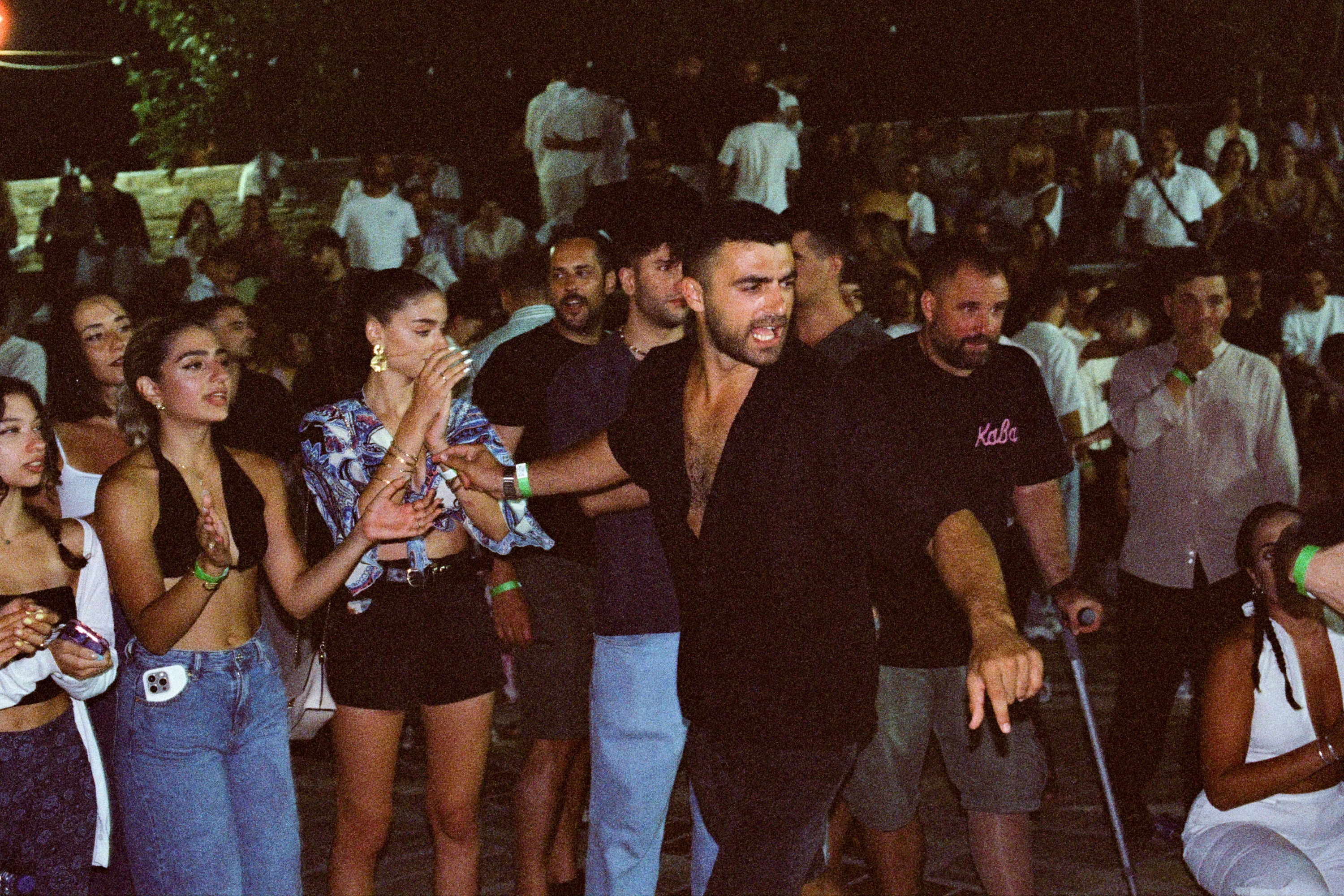 A crowd at a night festival, a man in black in the middle pointing past the camera