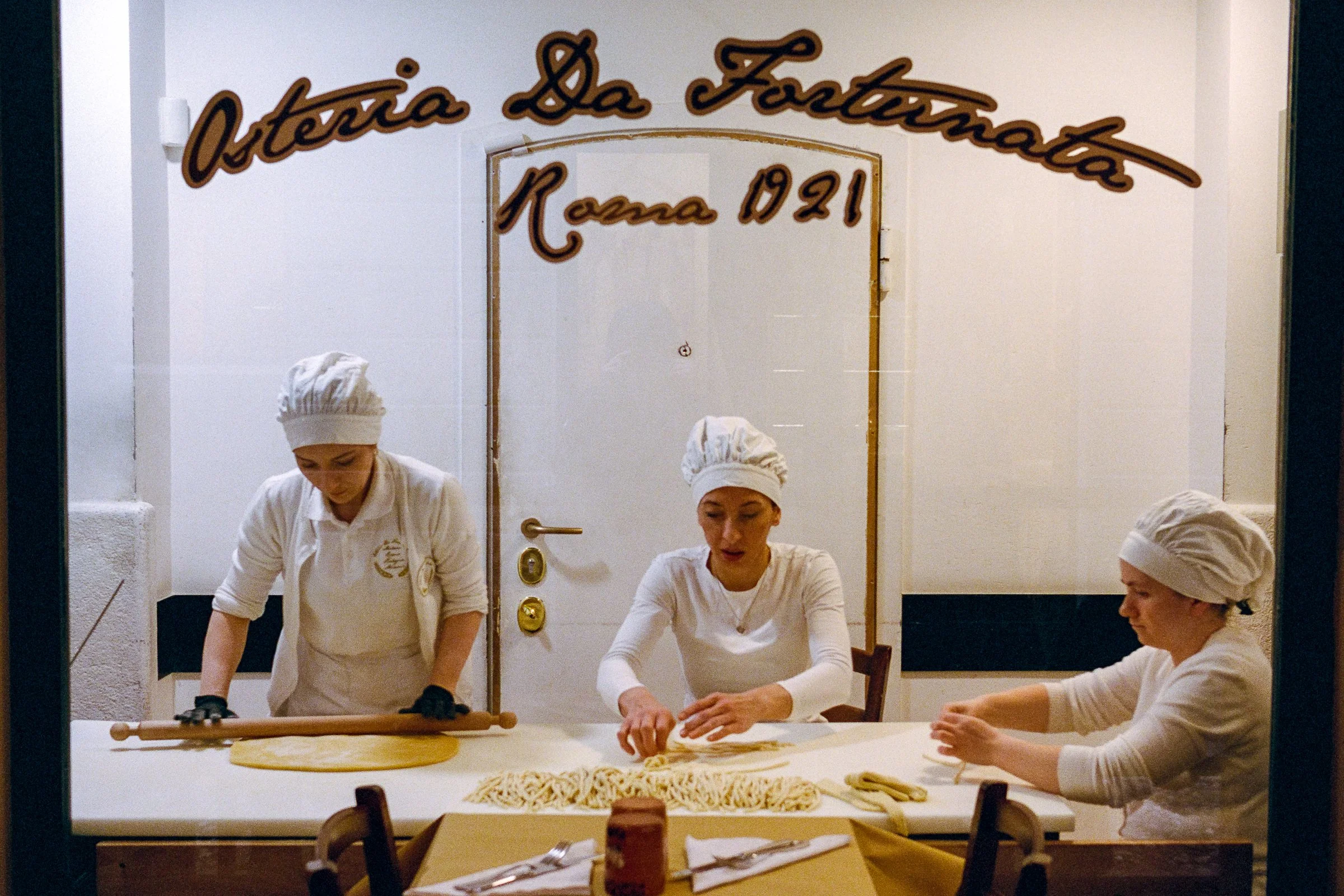 Women making pasta, seen through a shop window