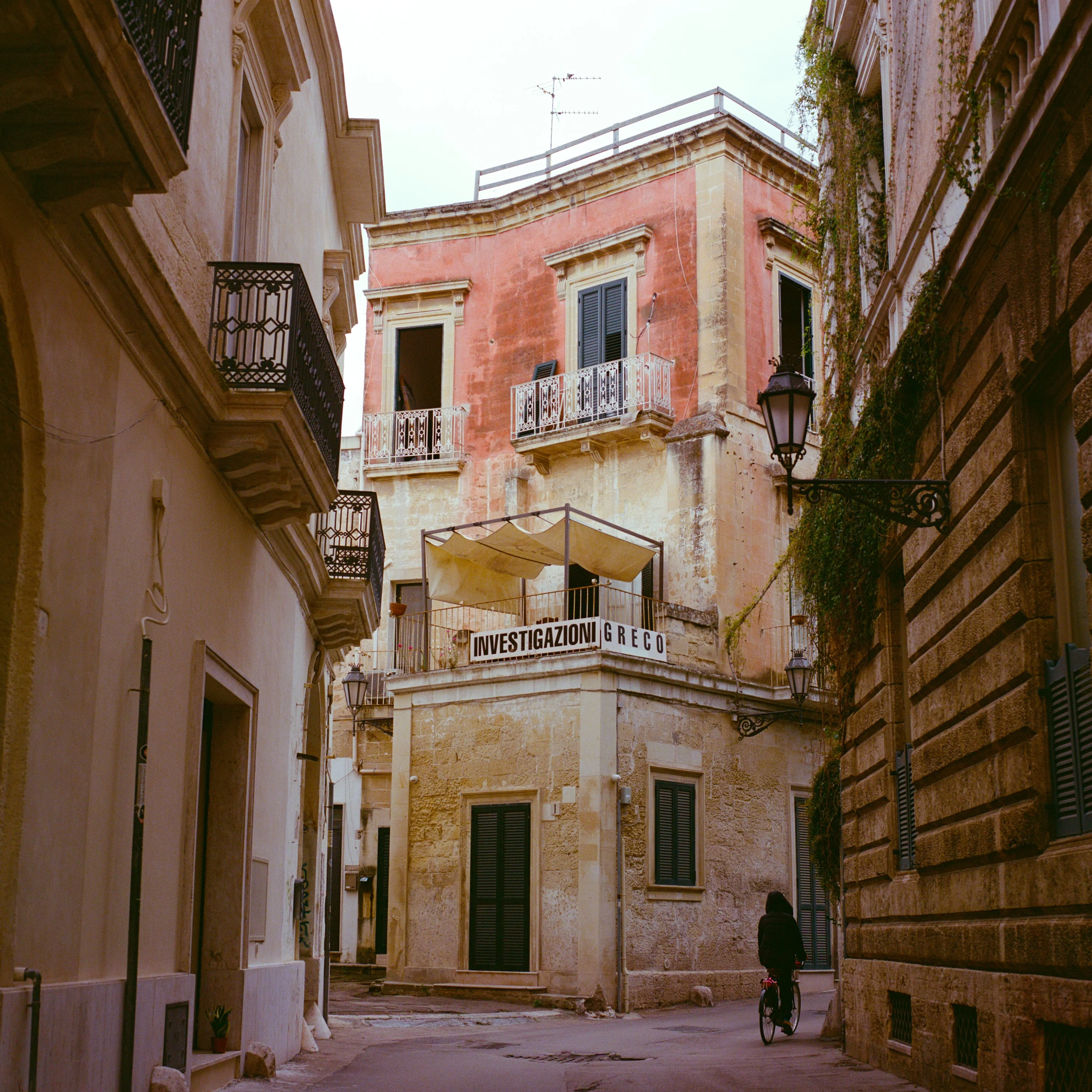 A faded pink villa on a quiet street corner, a cyclist passing