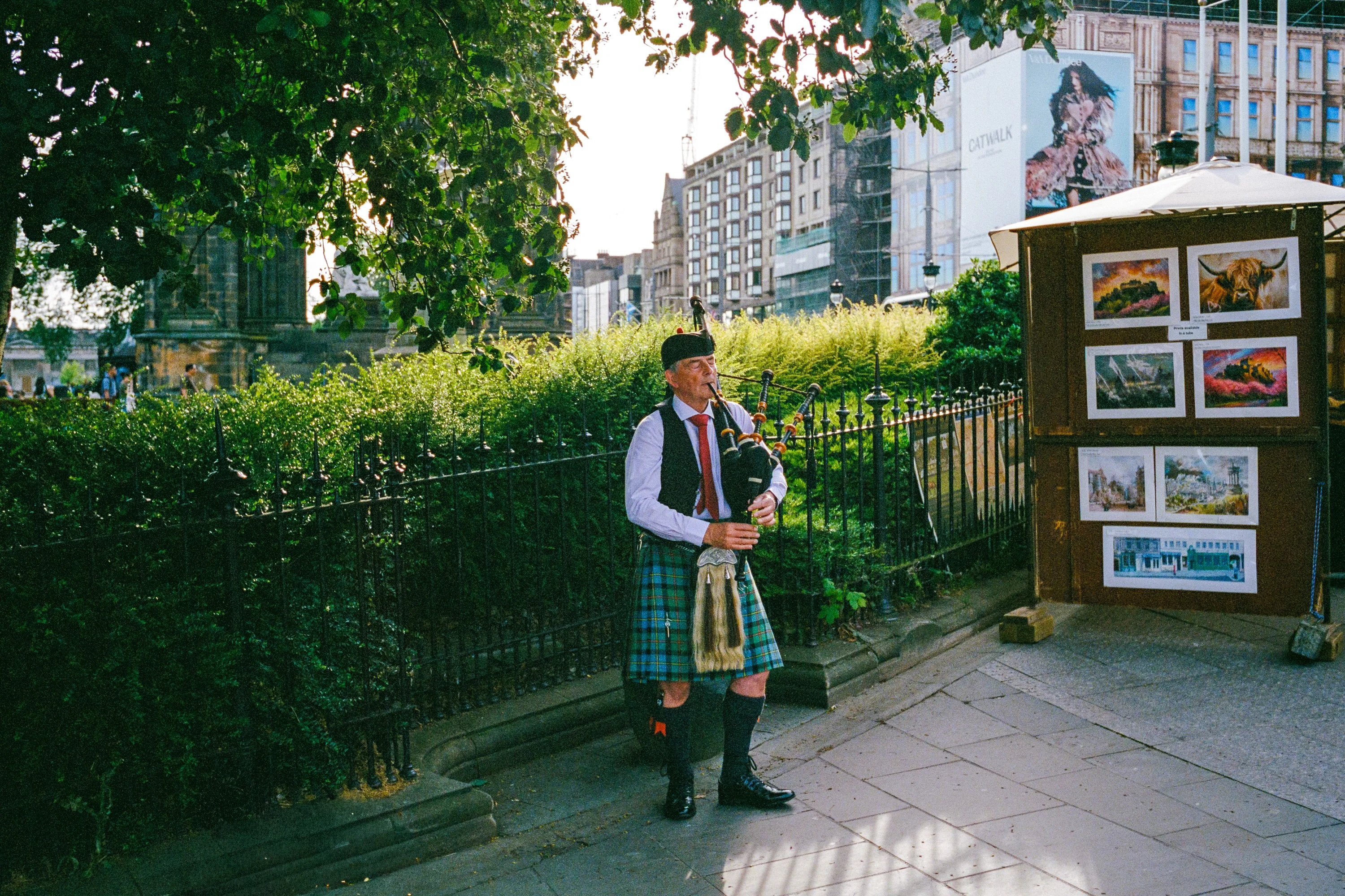 A piper playing on the street next to a painting stall