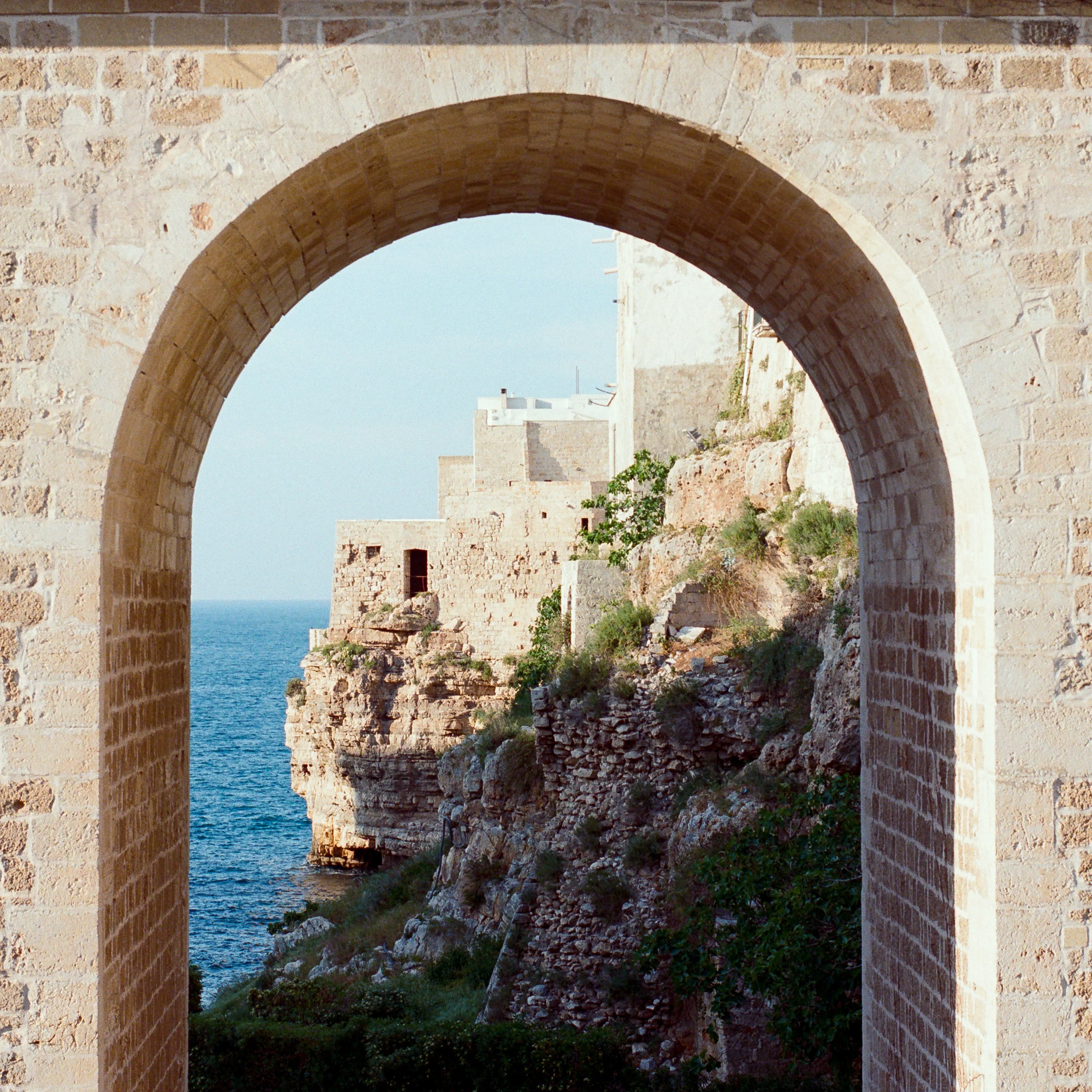 Cliffs and houses above the sea seen through a stone arch