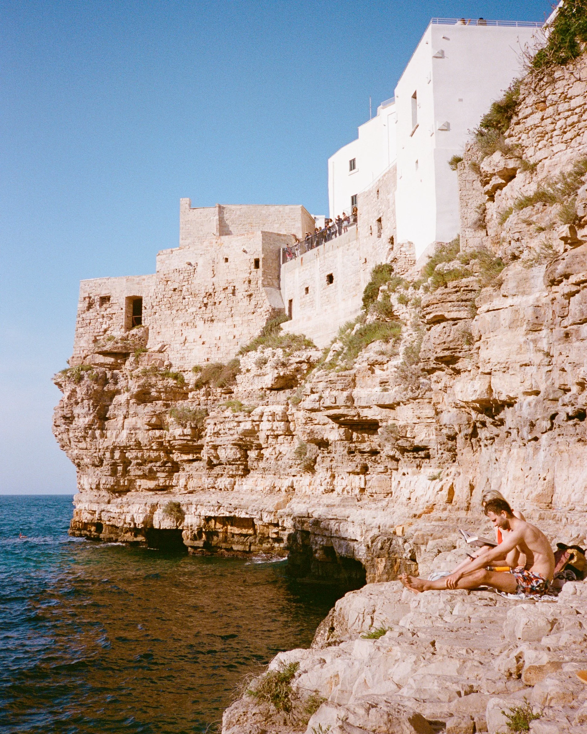 Limestone cliffs topped with white houses, a sunbather on the rocks above the sea