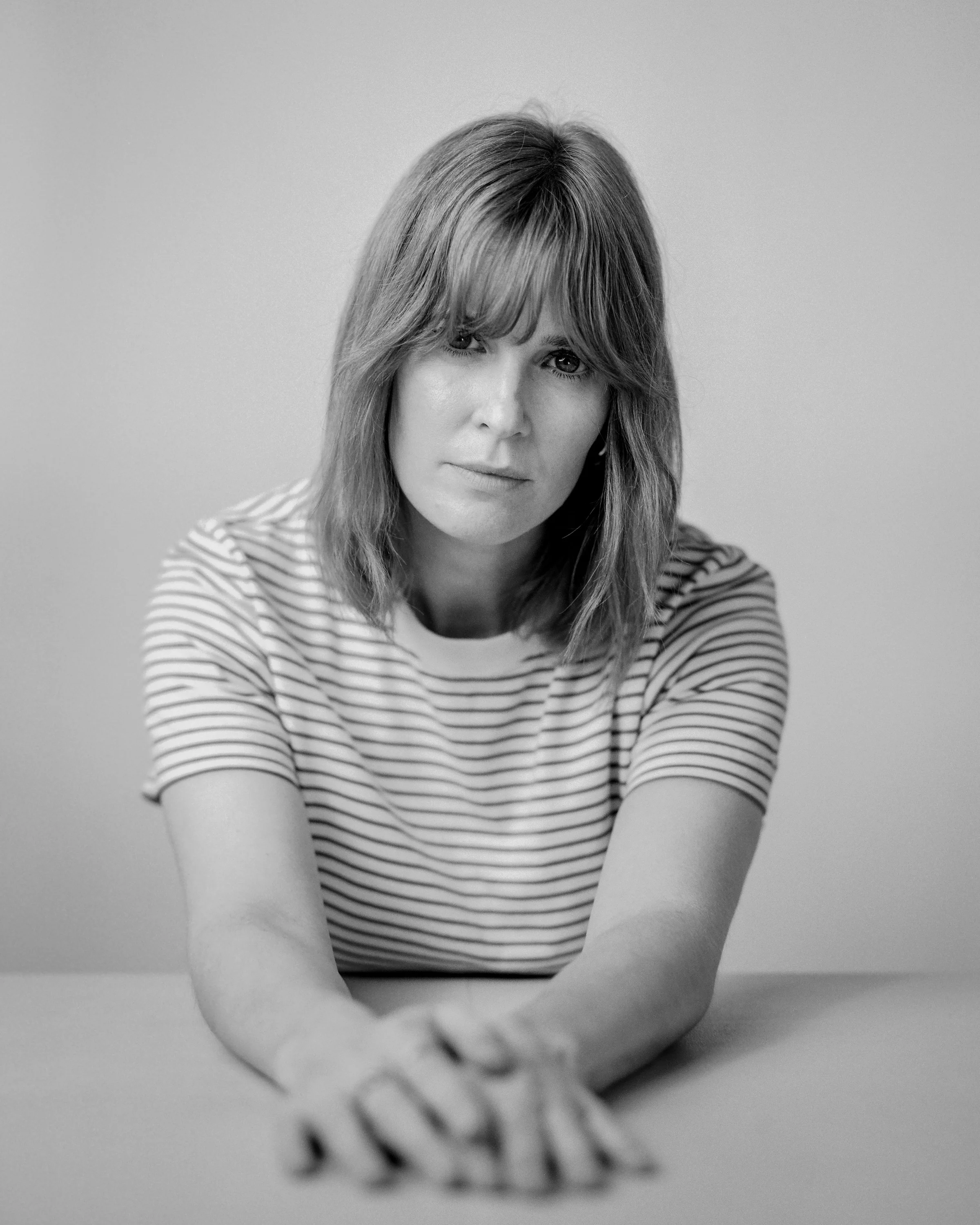 Black and white portrait of a woman in a striped t-shirt, hands folded on a table