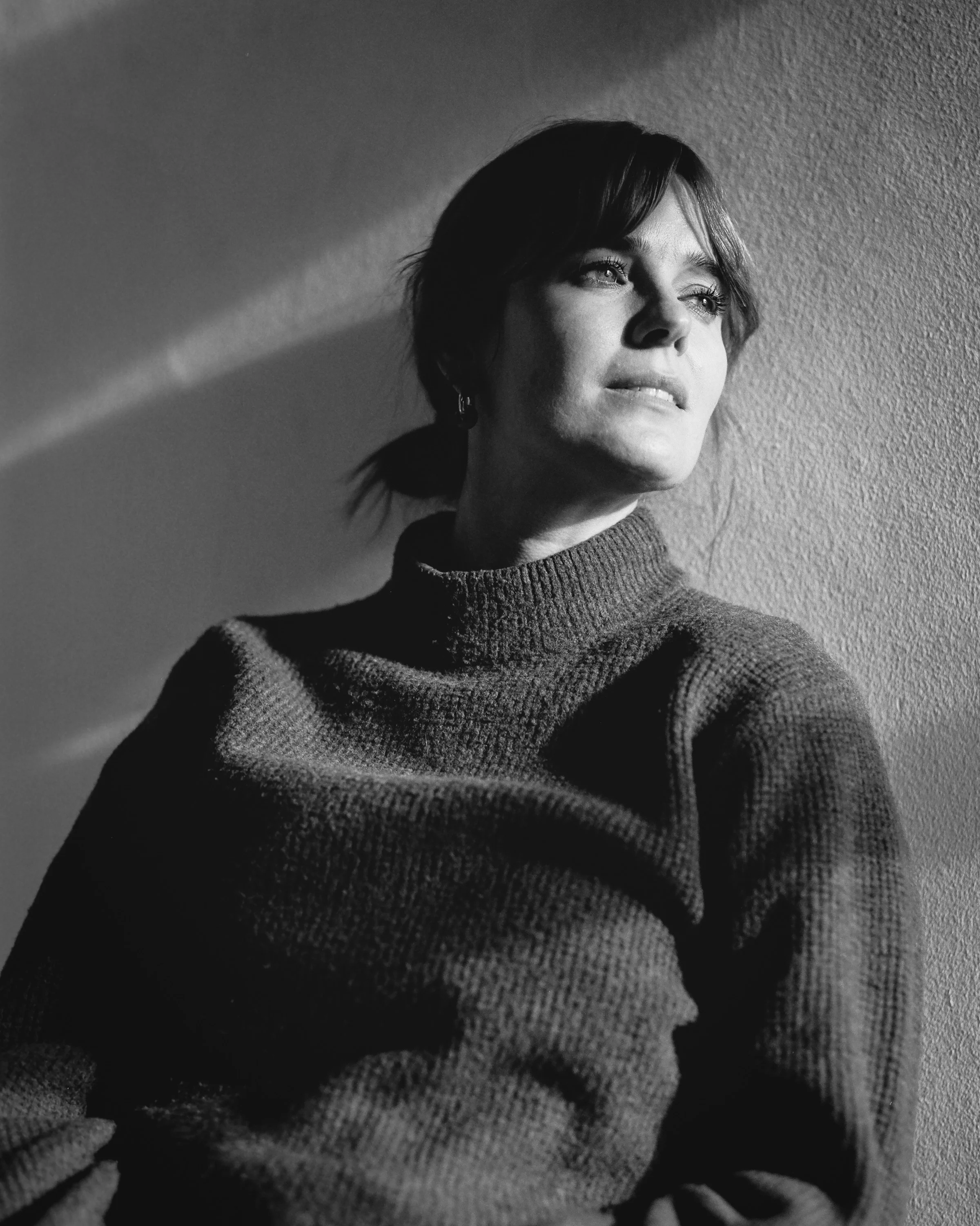 Black and white portrait of a woman in a dark jumper, lit by a strip of window light