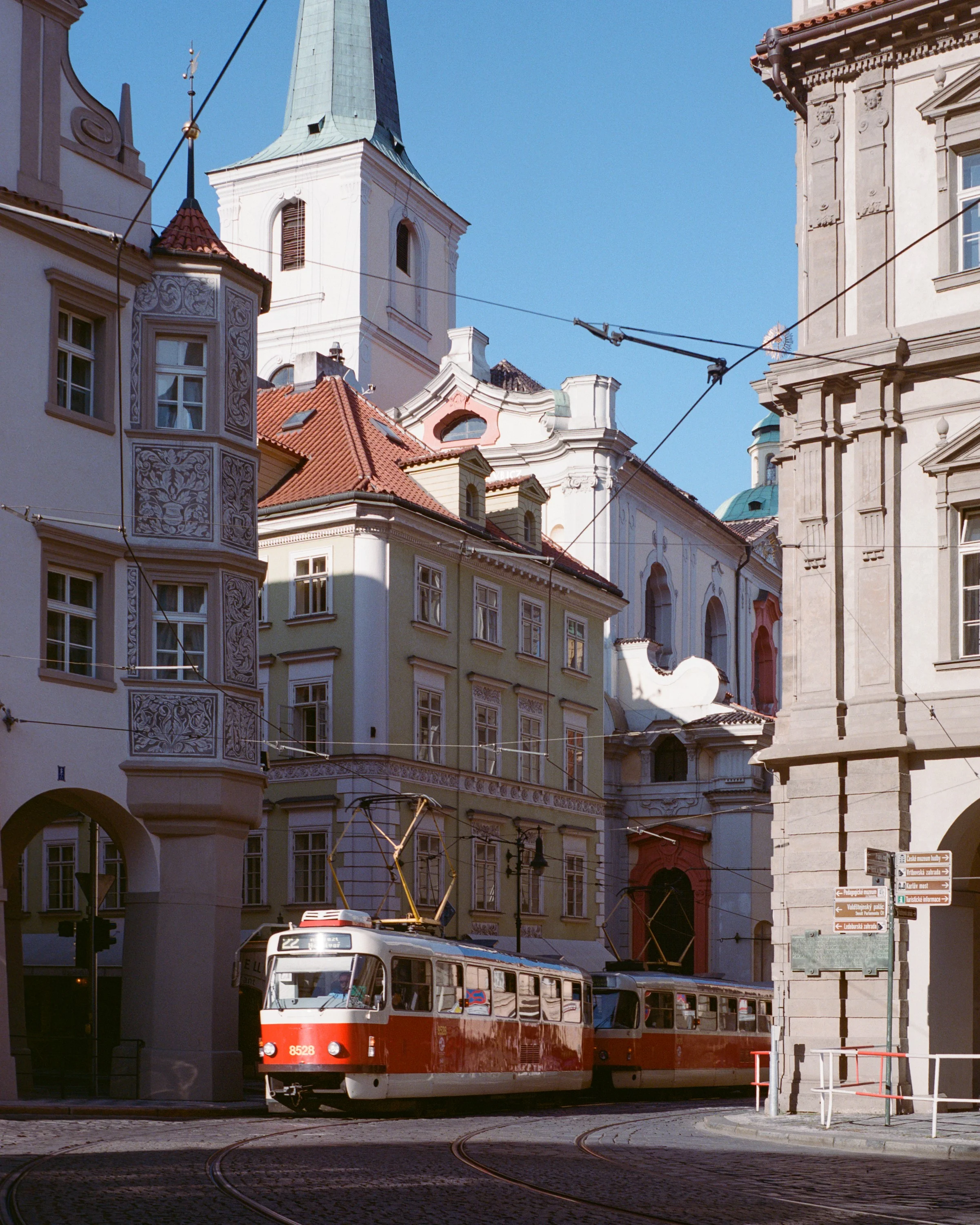 A red tram passing baroque buildings and a white church tower