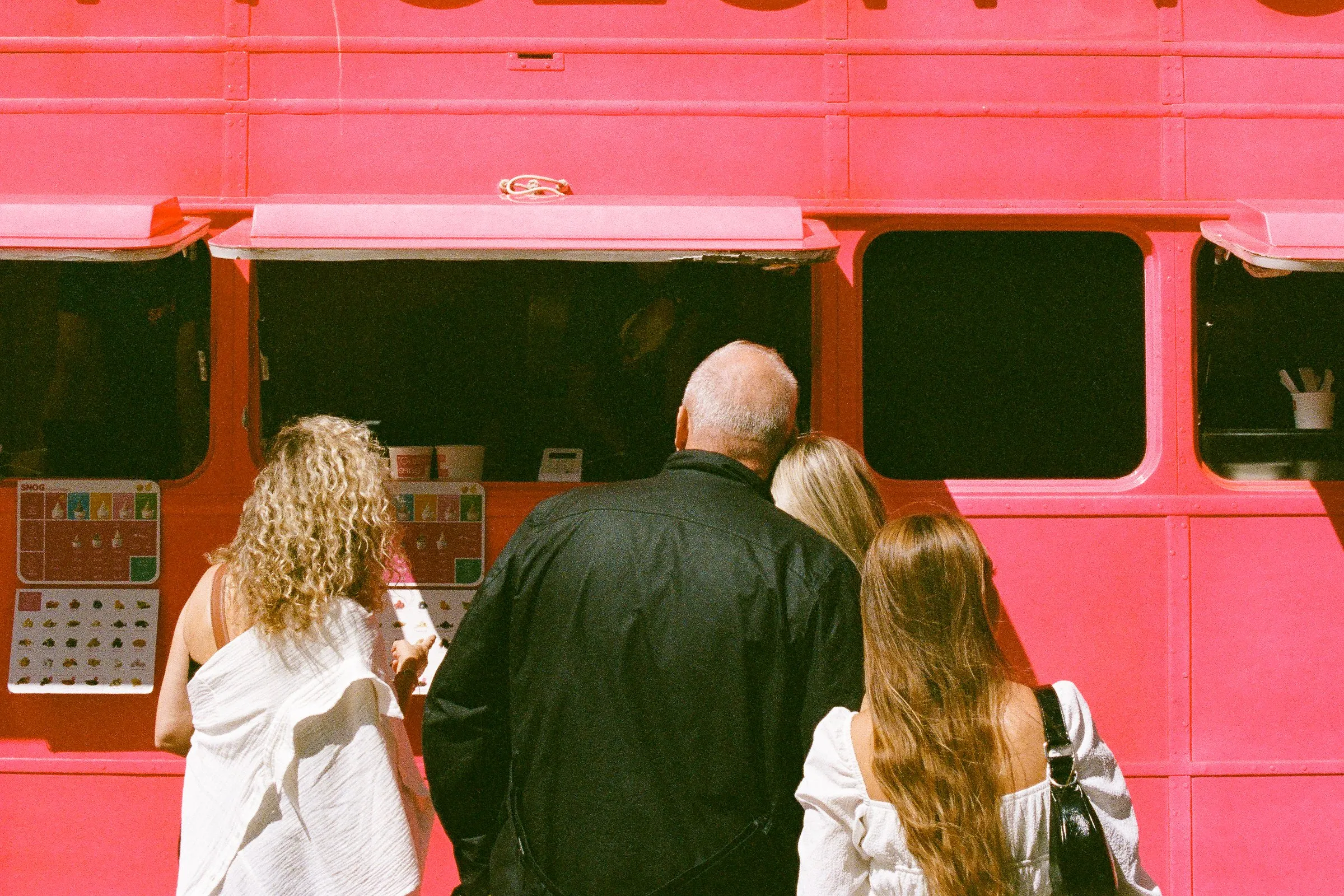People queuing beside the bright red side of a bus