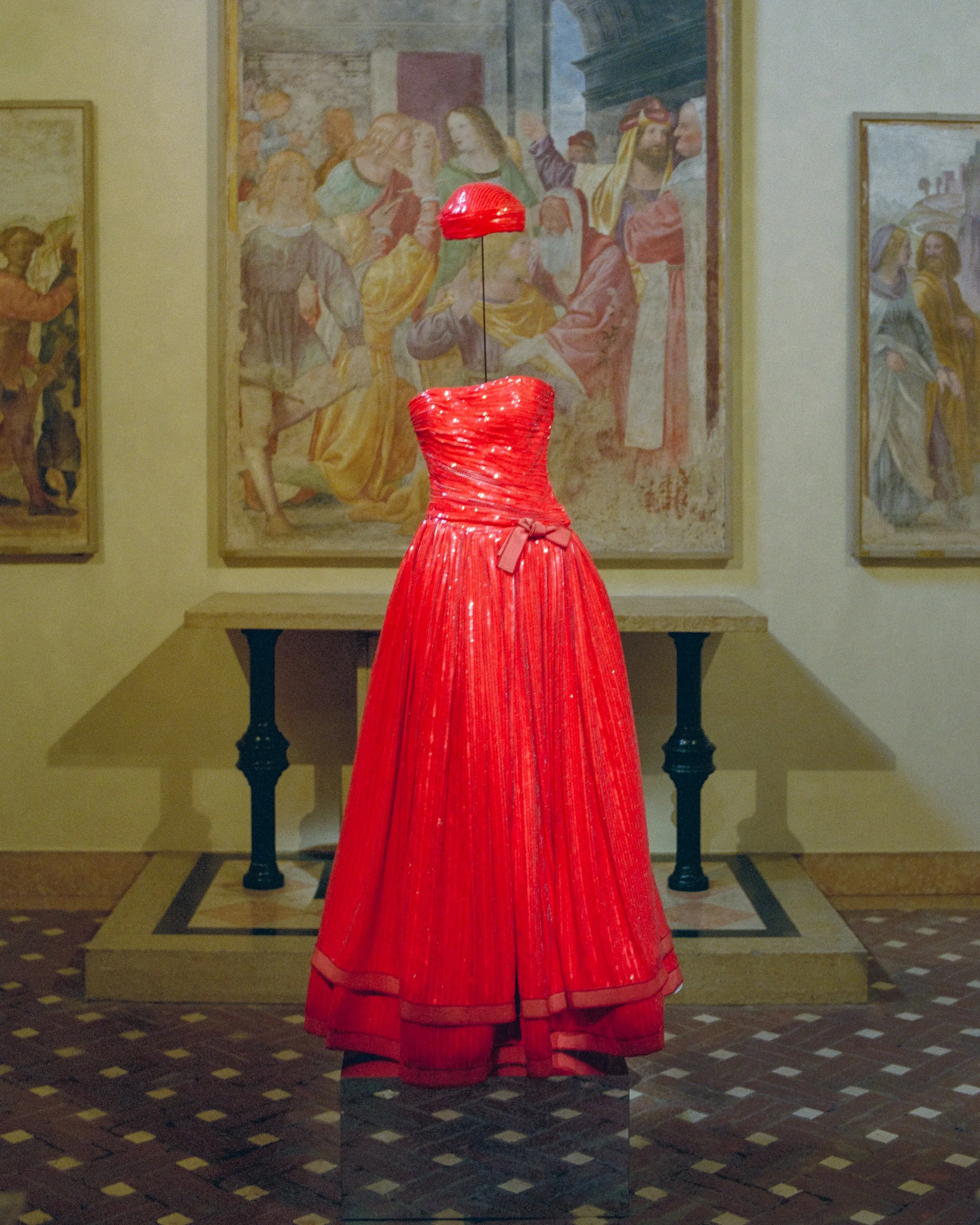 A red ball gown on display in front of a fresco