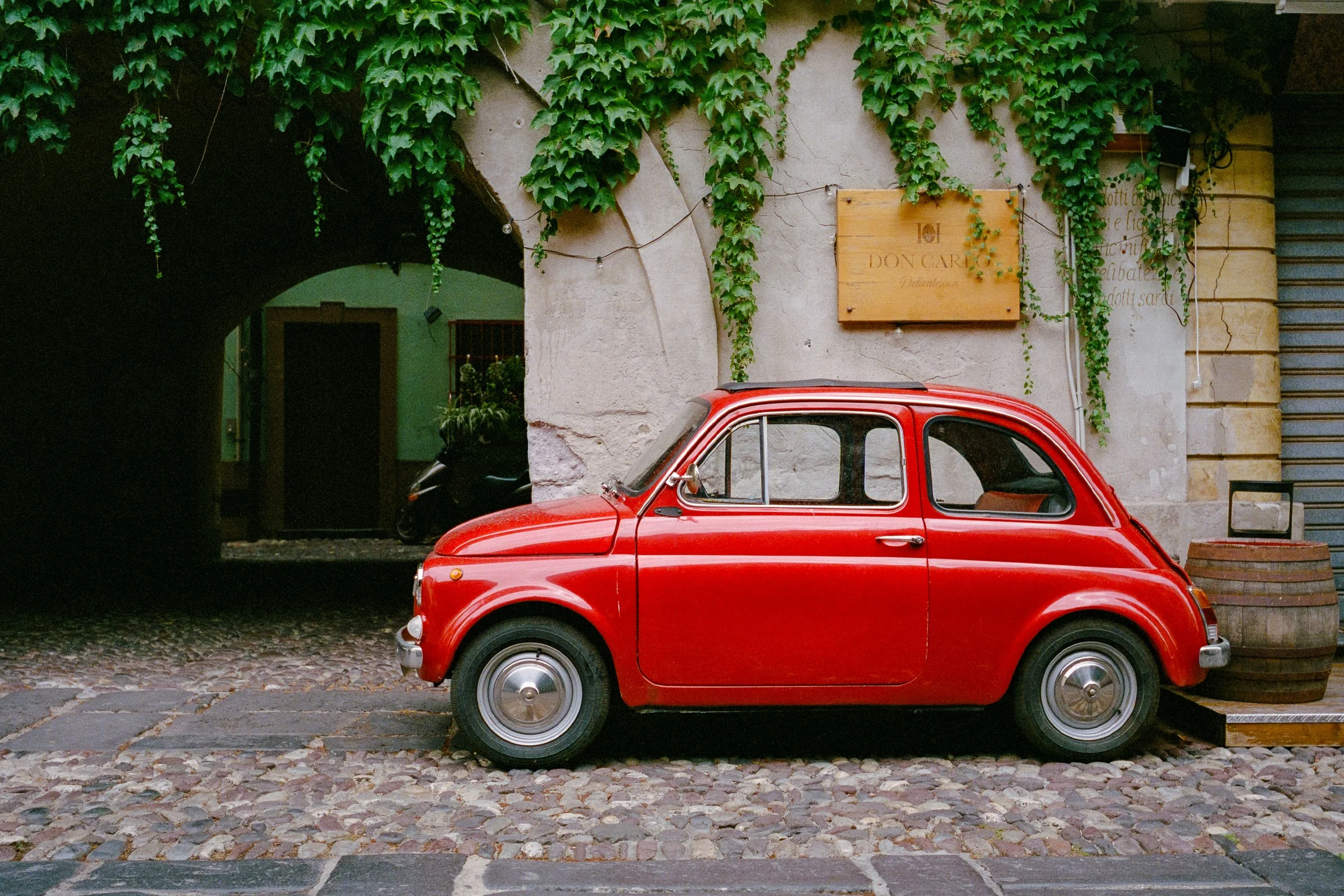 A red Fiat 500 parked on cobbles beneath ivy-covered walls