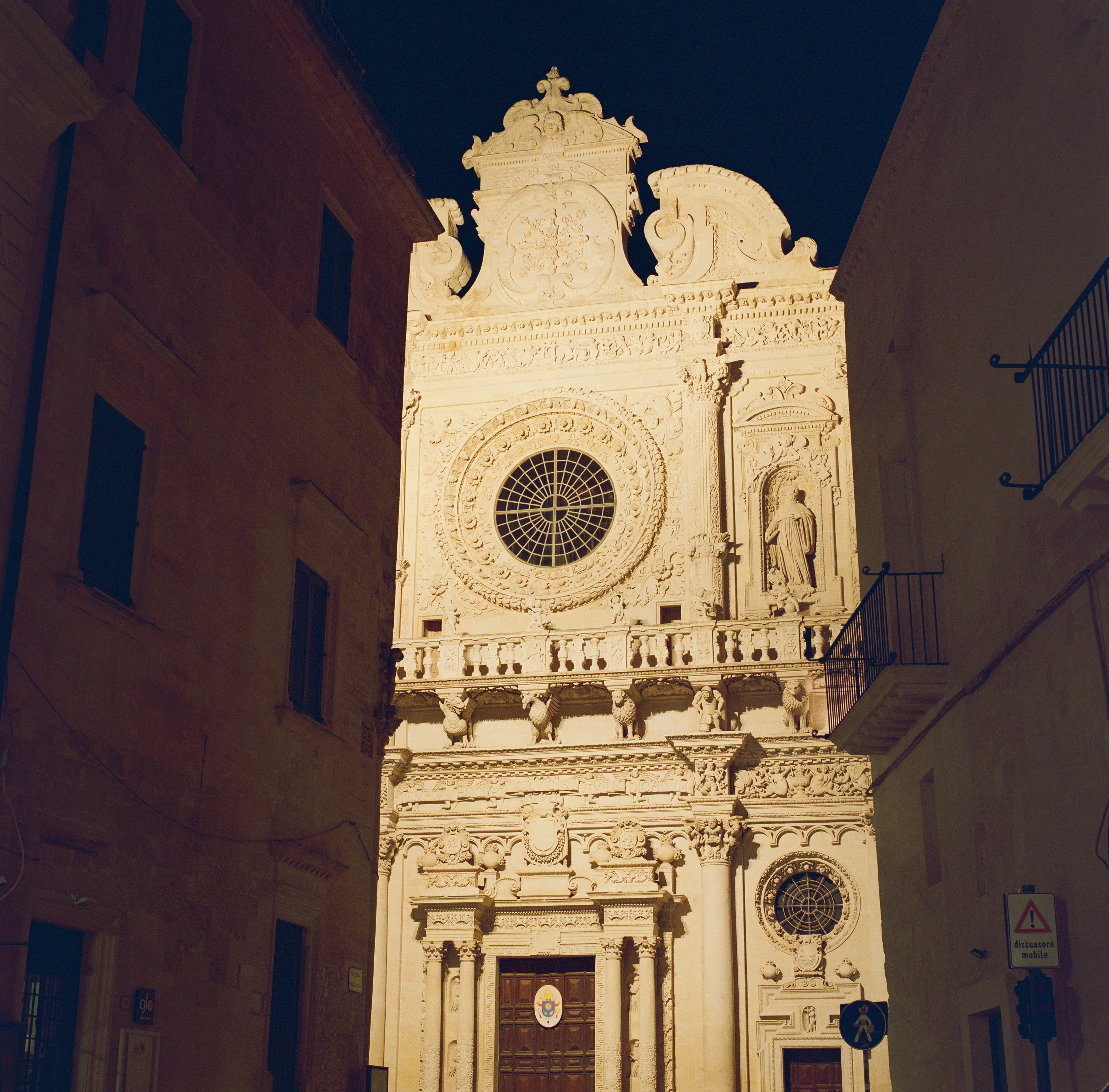 The baroque facade of Santa Croce lit at night at the end of a narrow street