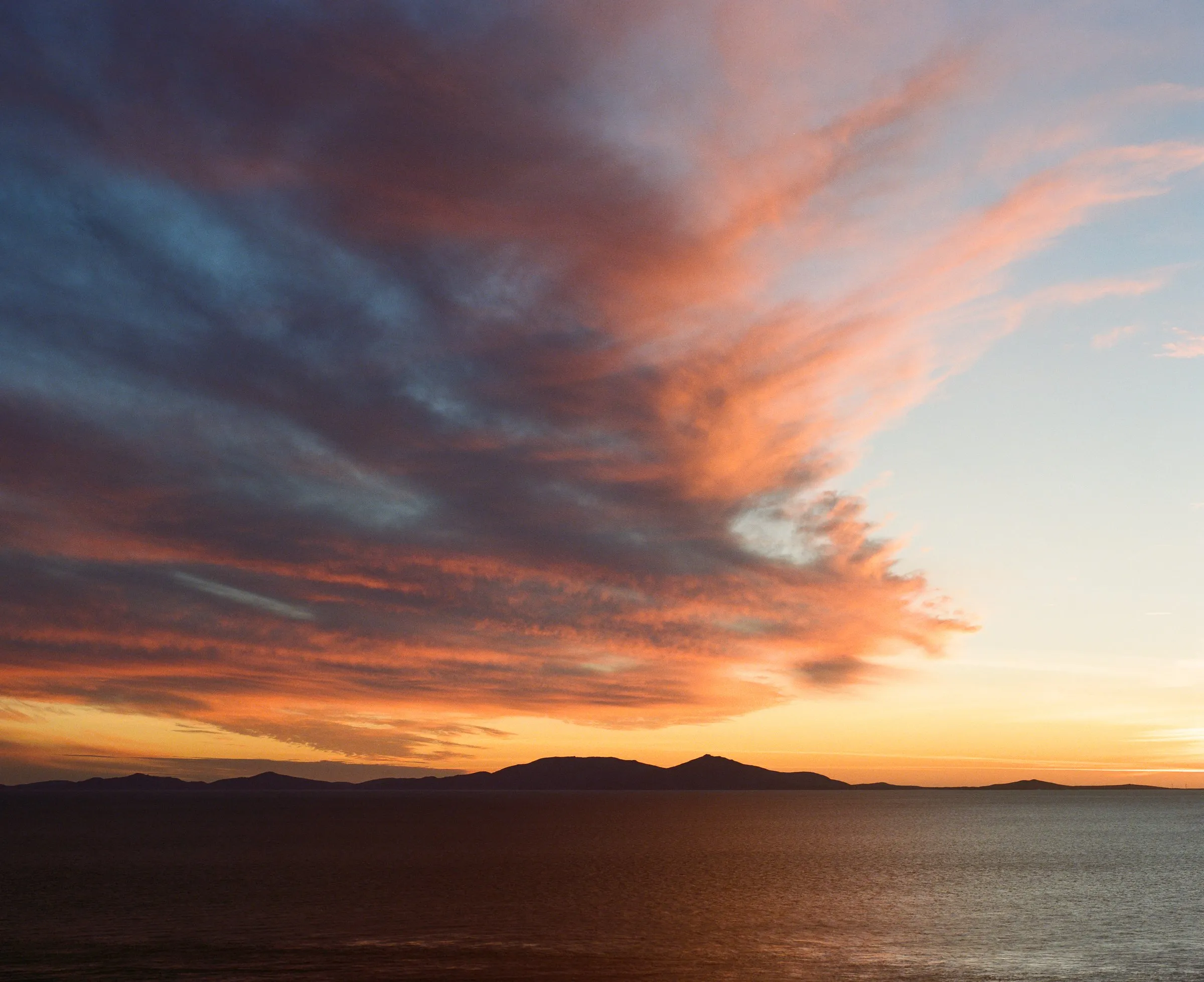 Orange and blue clouds over the sea at sunset, with distant islands on the horizon