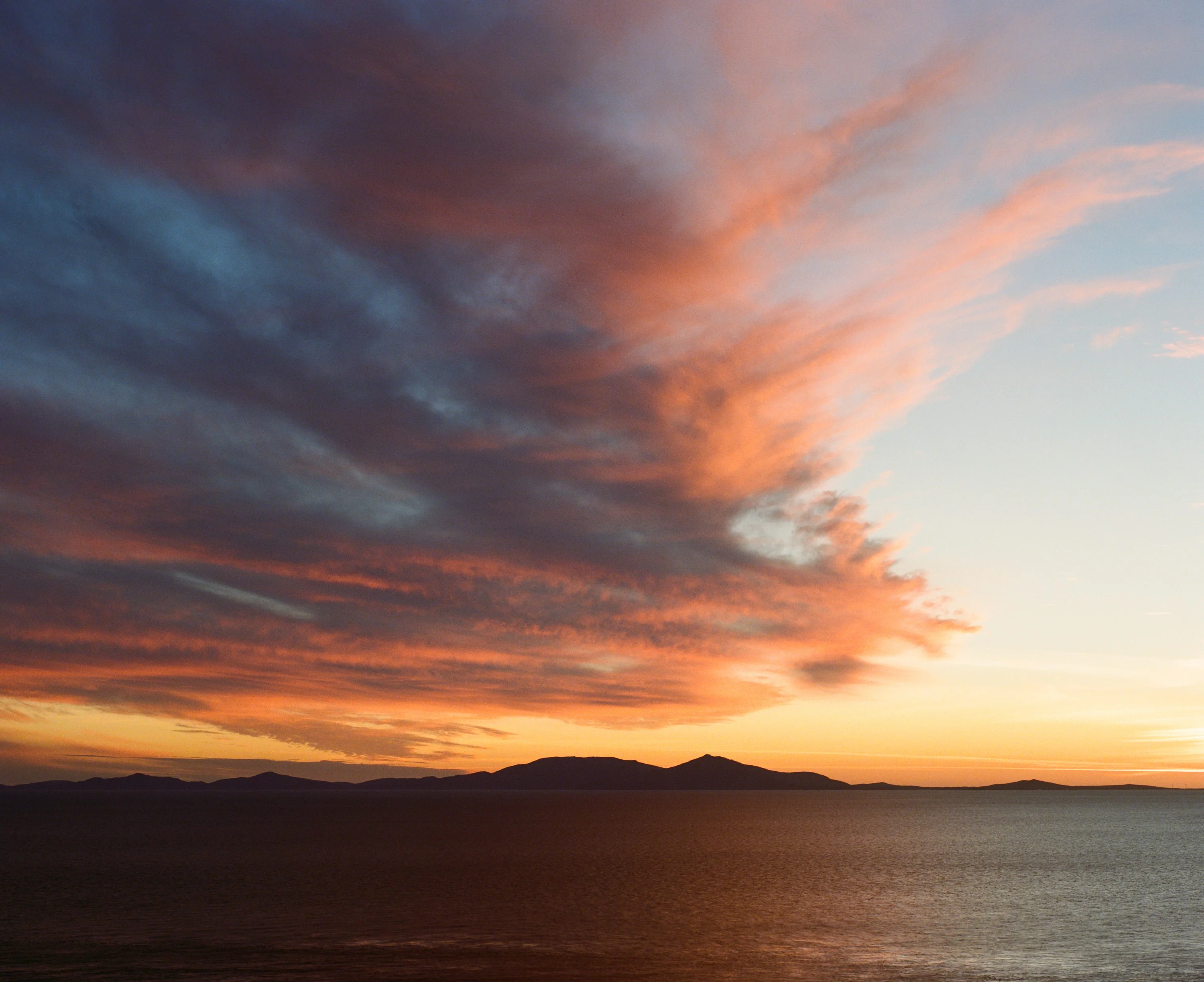 Orange and blue clouds over the sea at sunset, with distant islands on the horizon