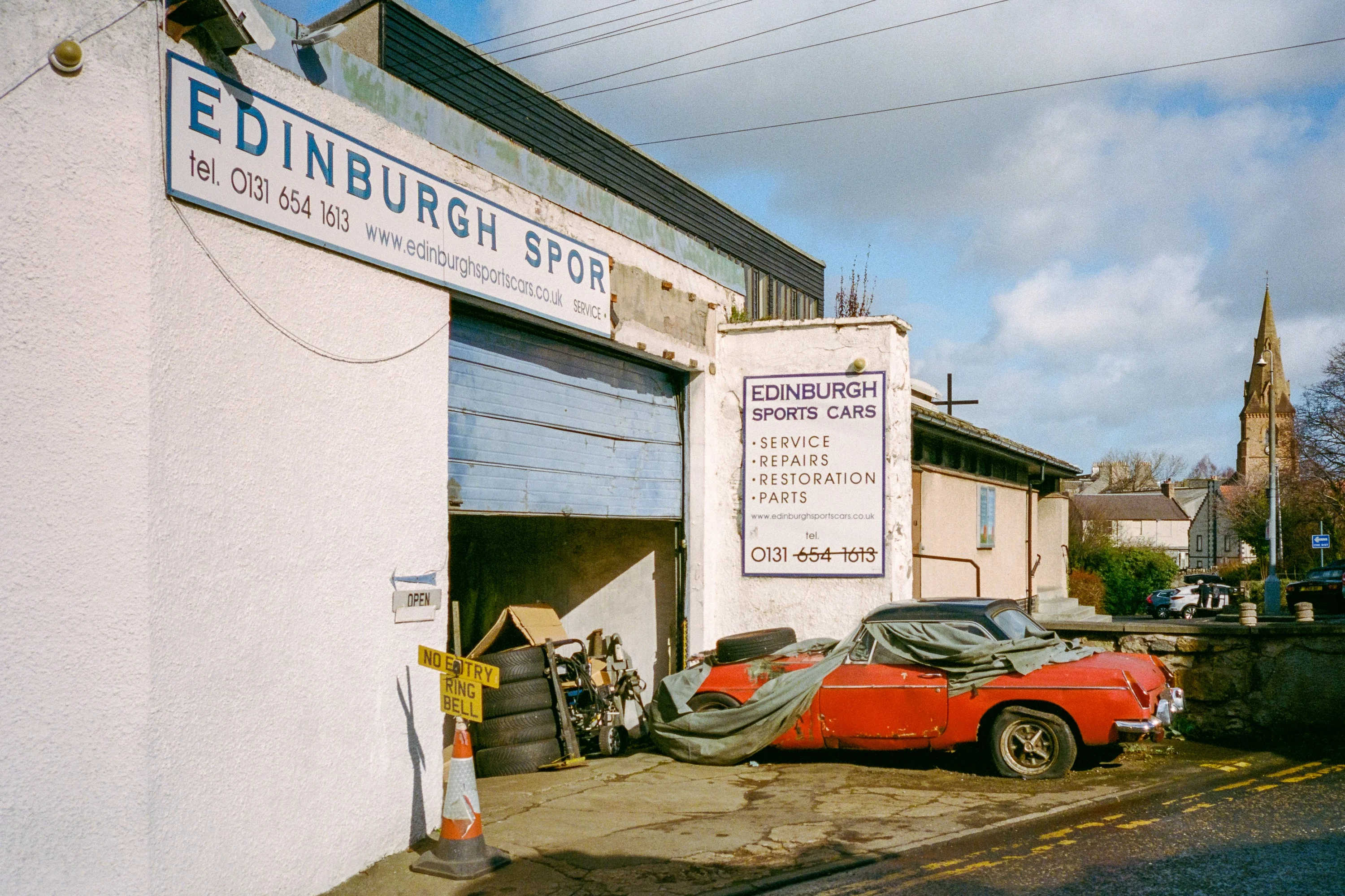 An old red sports car outside a garage sign reading Edinburgh Sports Cars
