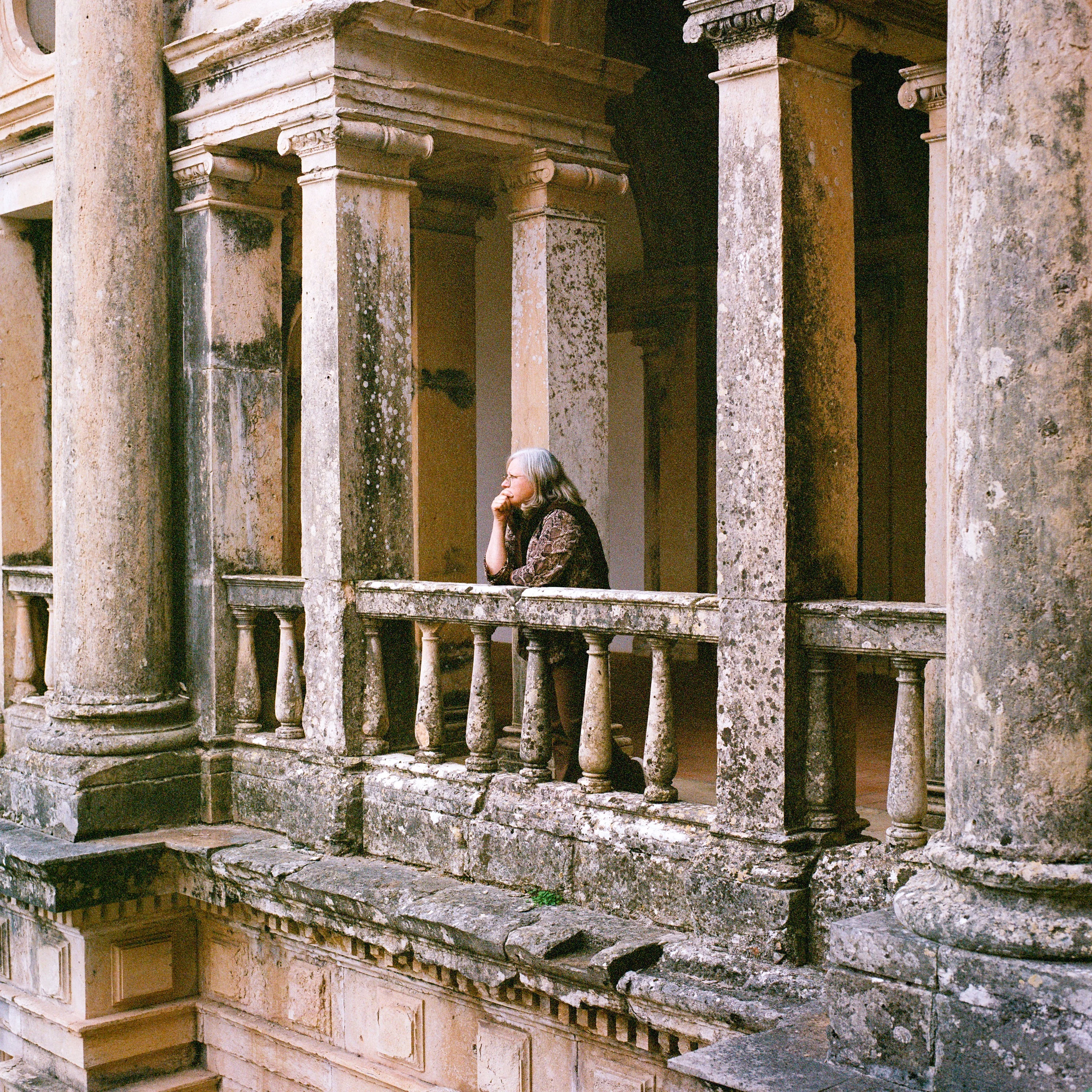 A woman resting on a mossy stone balustrade between columns