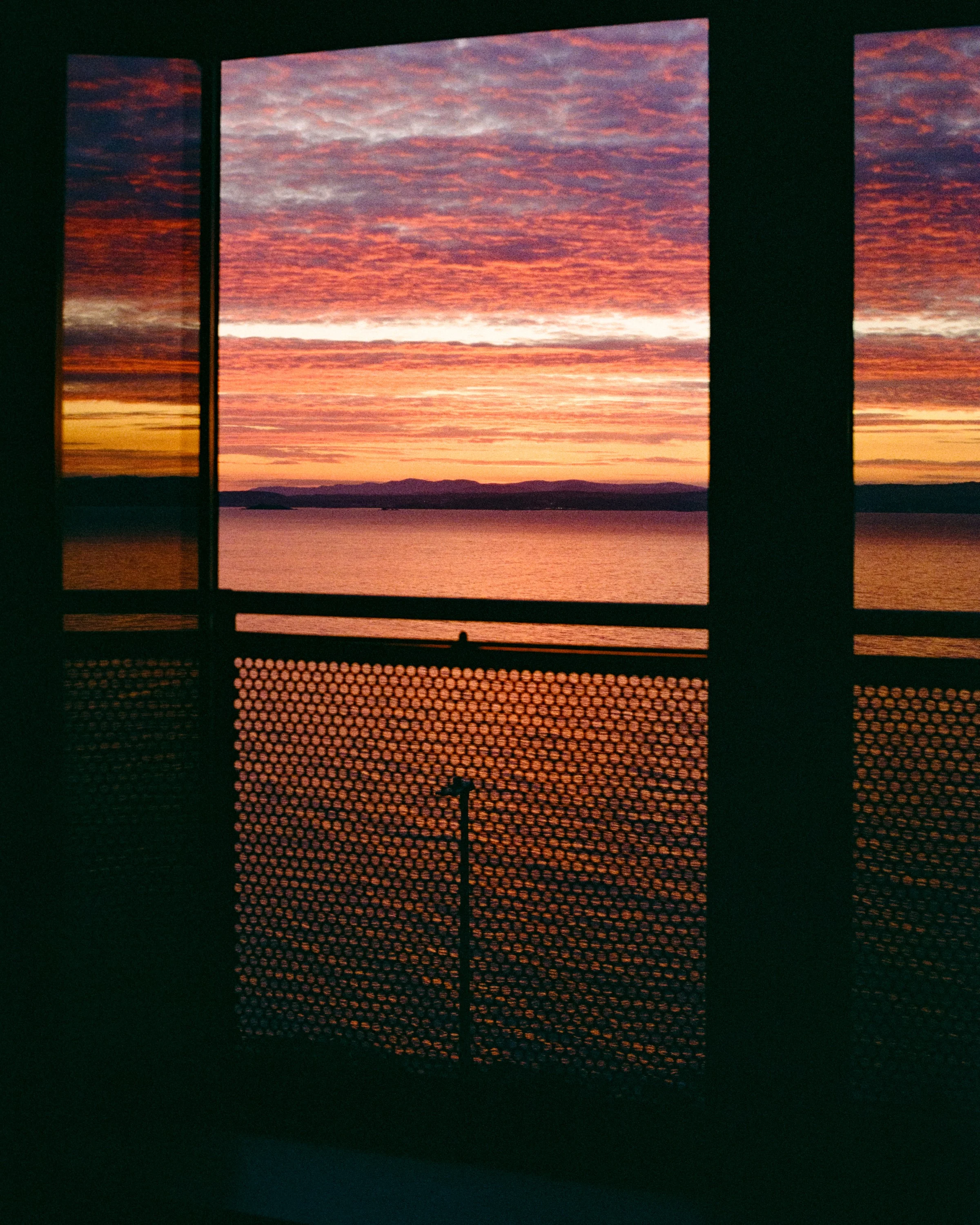 A red sunset seen through a dark window grille