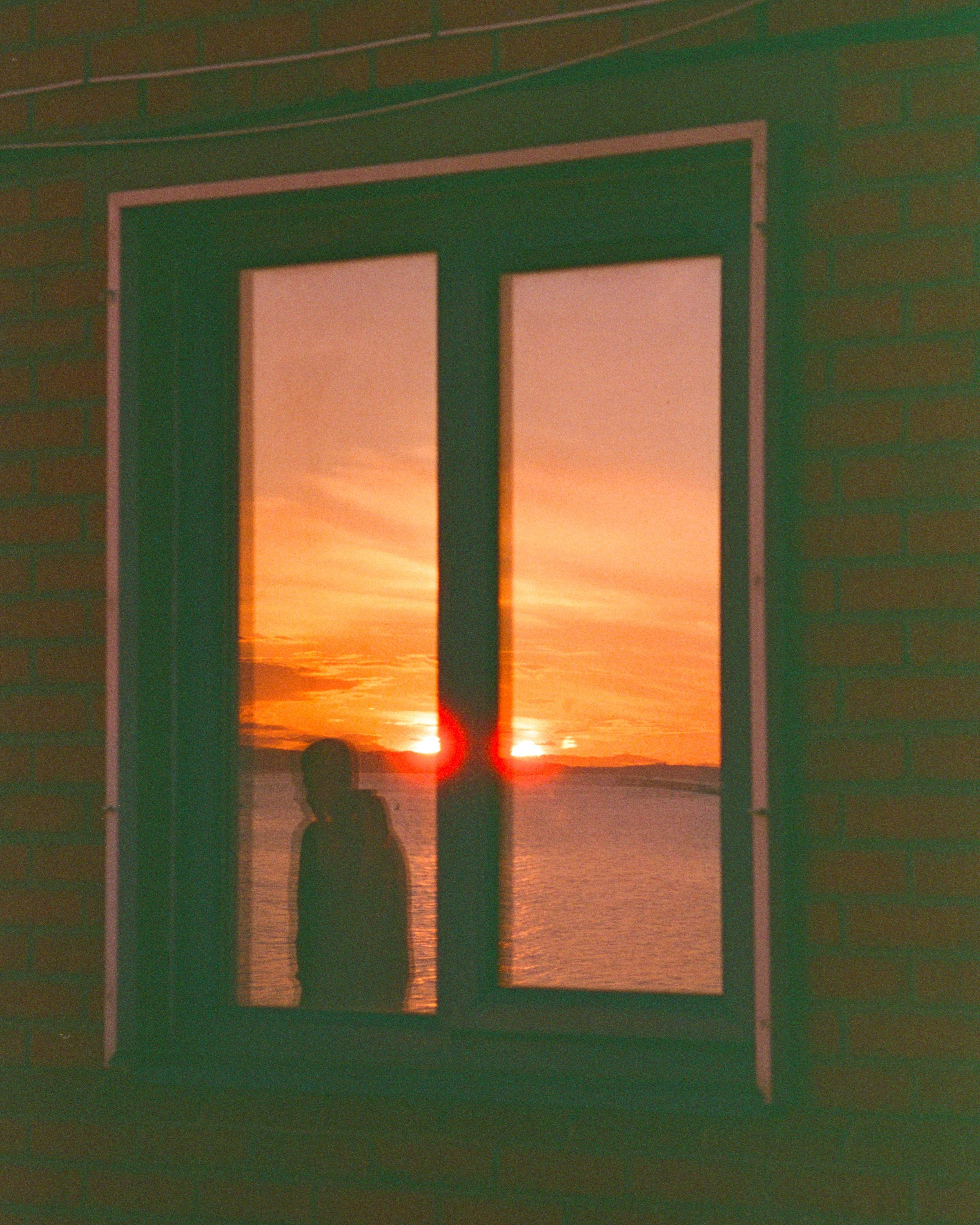 An orange sunset reflected in a dark window with a silhouette