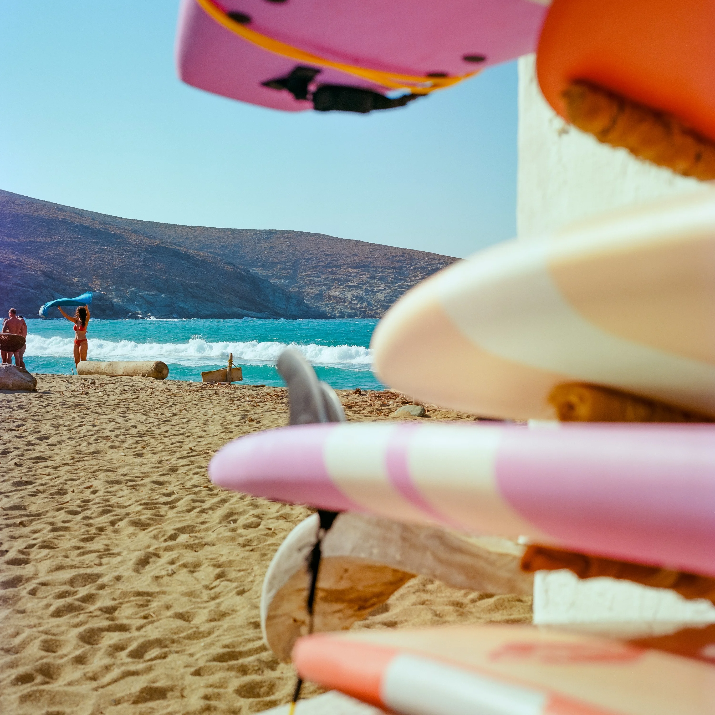 Pink and white surfboards stacked against a wall above a sandy beach