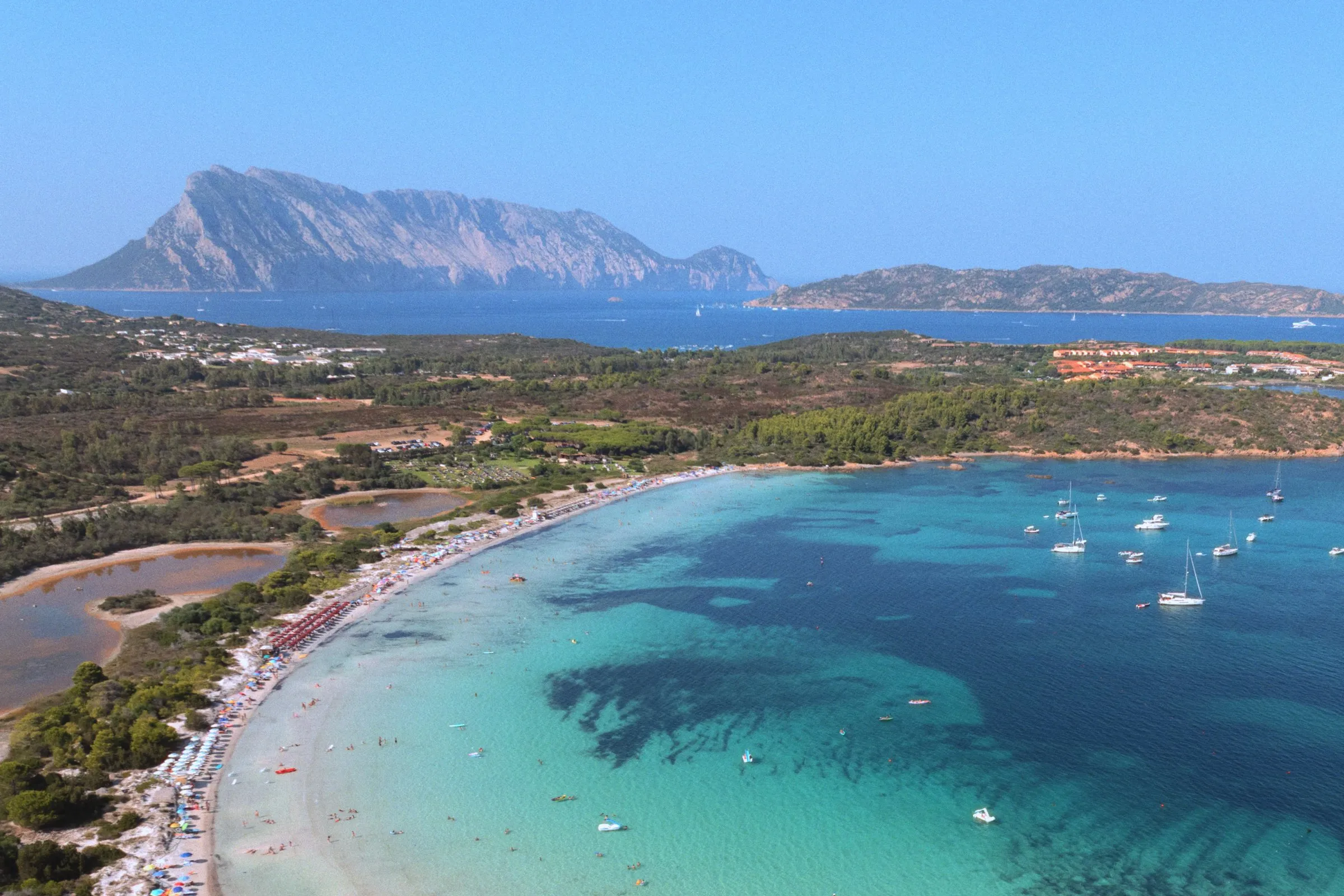 A long curve of white sand and turquoise water, with the island of Tavolara rising behind