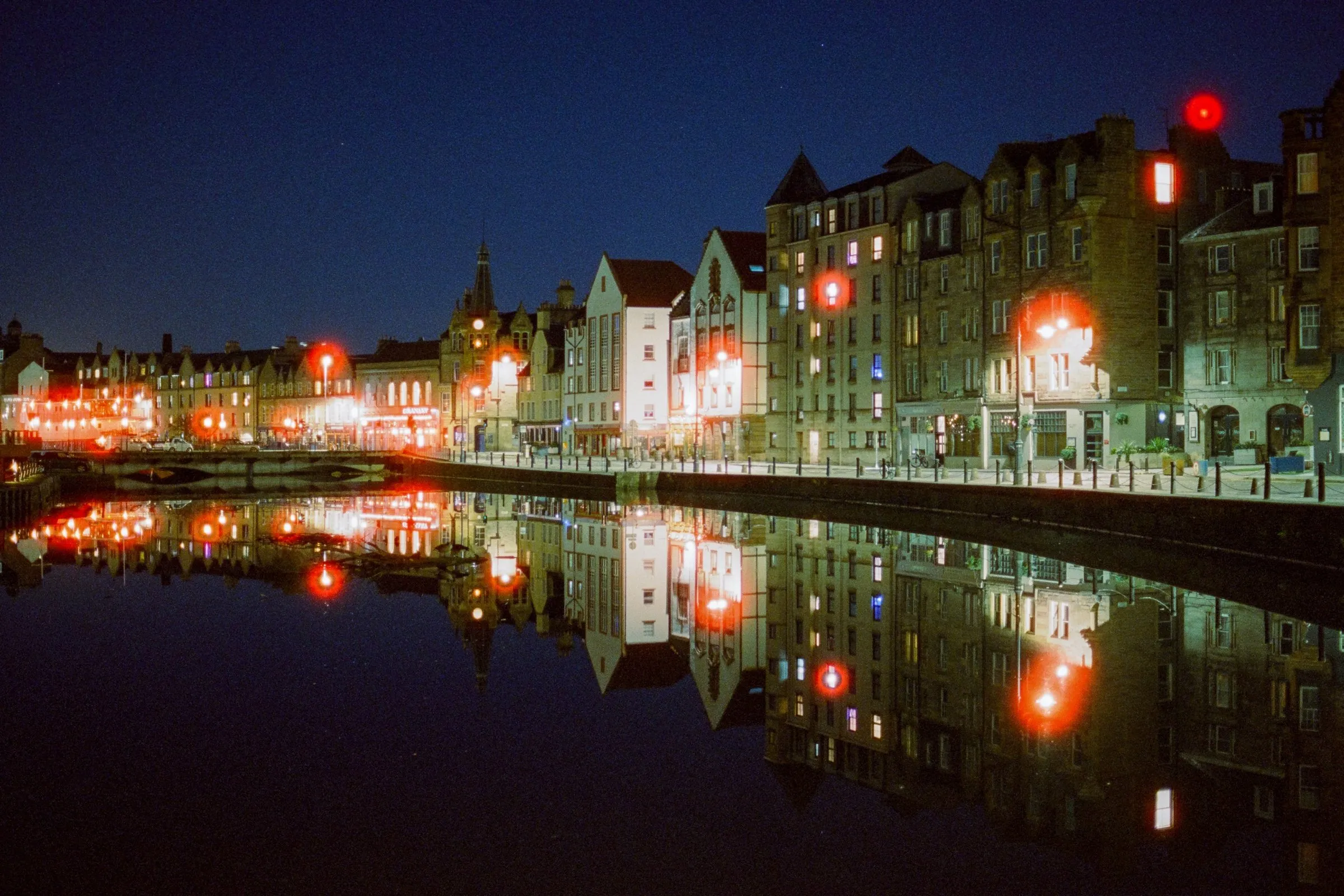 The Shore in Leith at night, lit tenements and red street lamps mirrored in still water