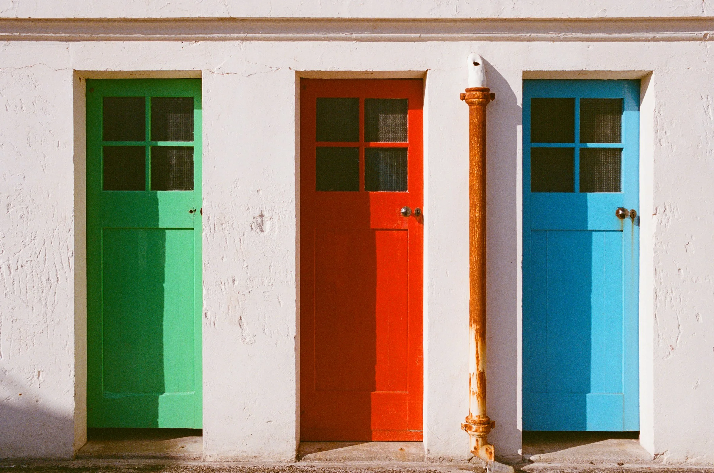 Green, red and blue doors set in a whitewashed wall