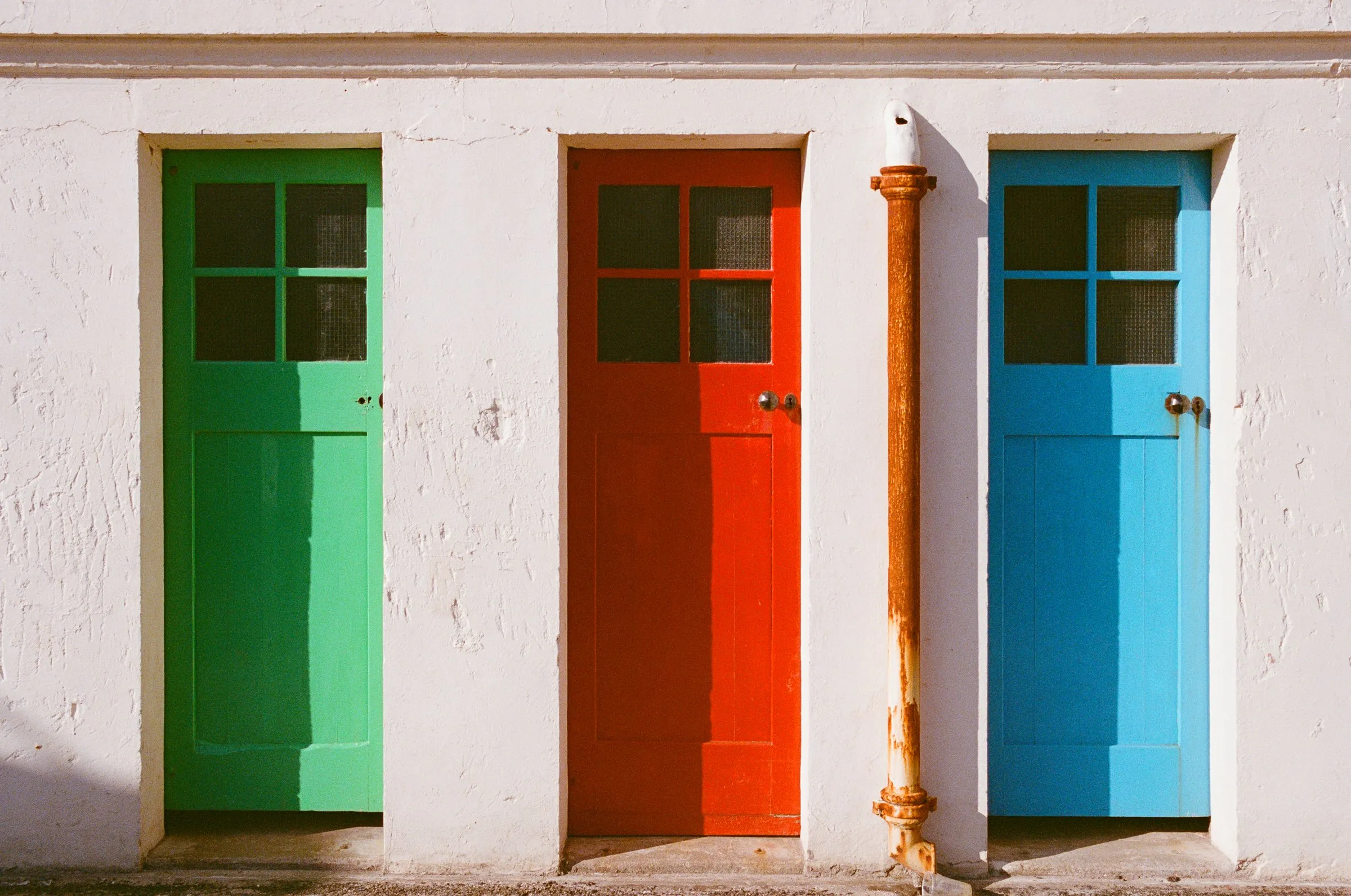 Green, red and blue doors set in a whitewashed wall