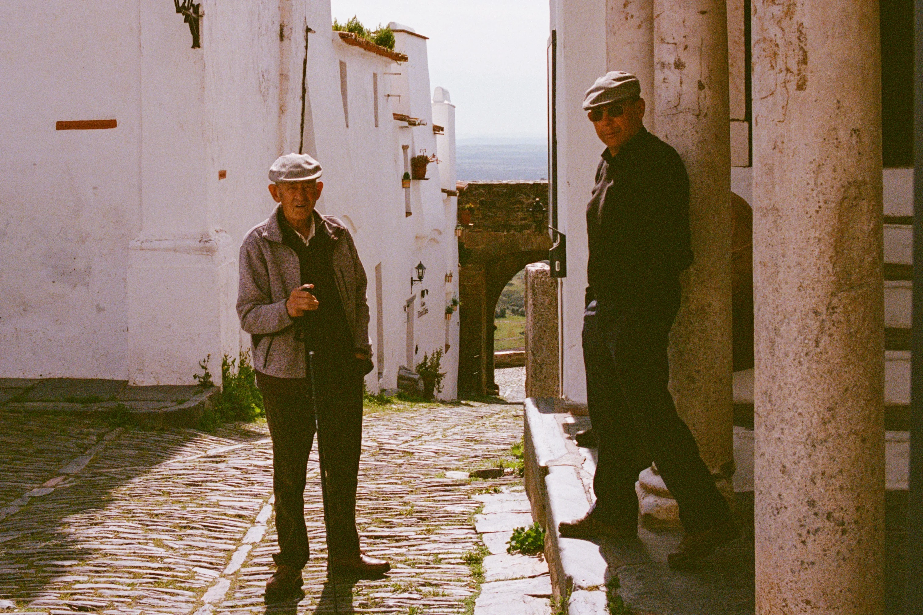 Two old men by columns on a sunlit street