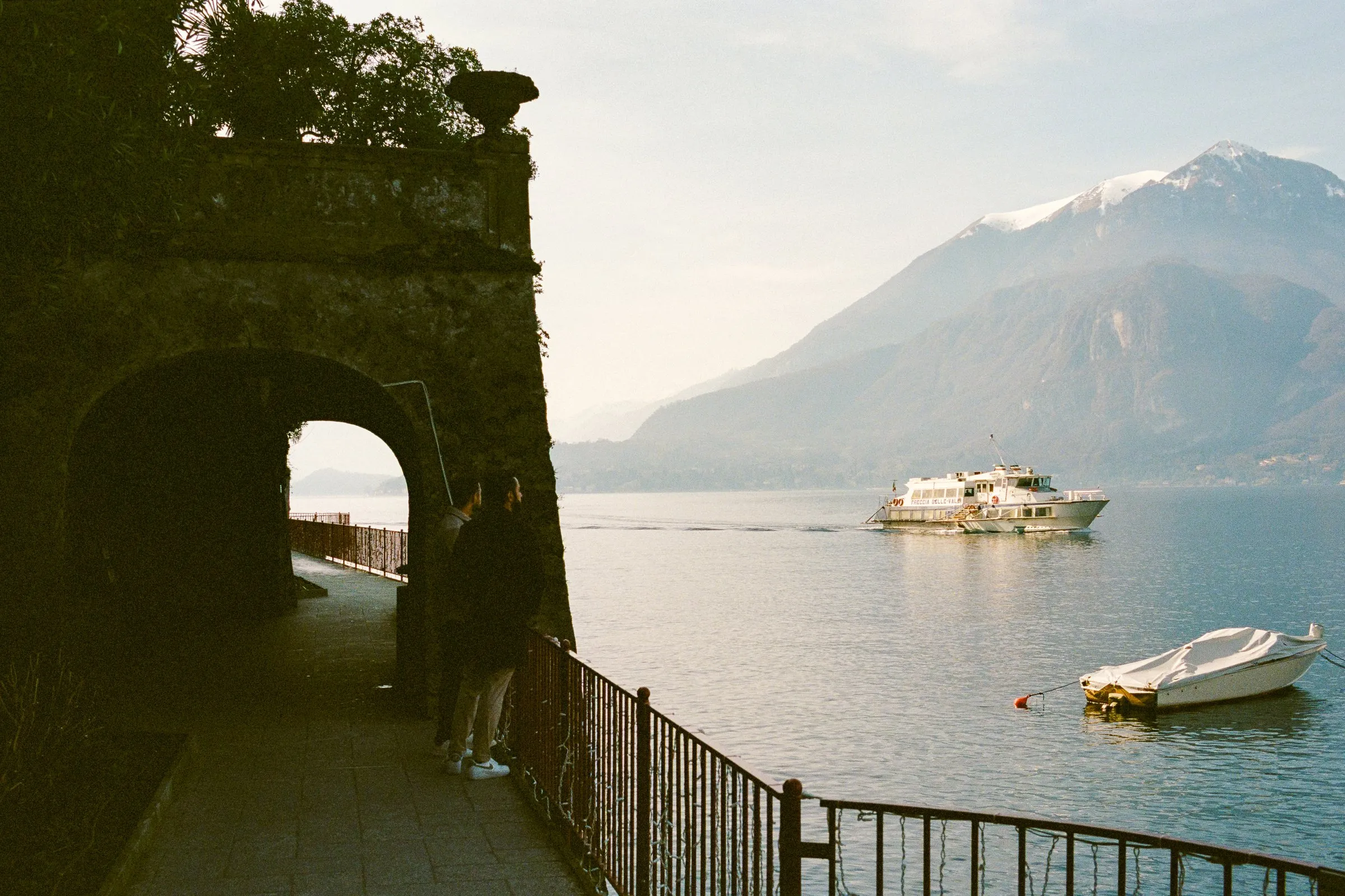 Lake Como and its mountains seen through a dark stone opening, with a ferry crossing the water