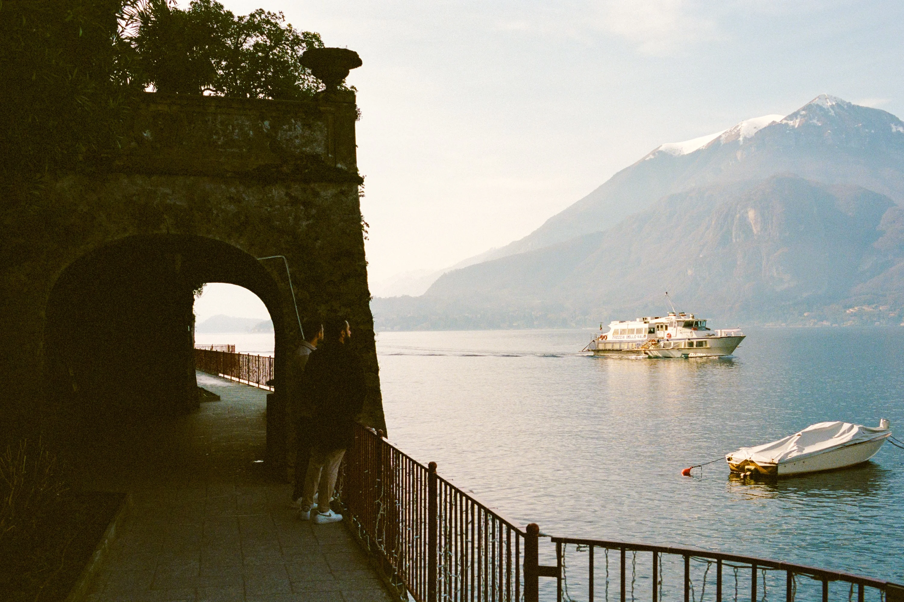 Lake Como and its mountains seen through a dark stone opening, with a ferry crossing the water