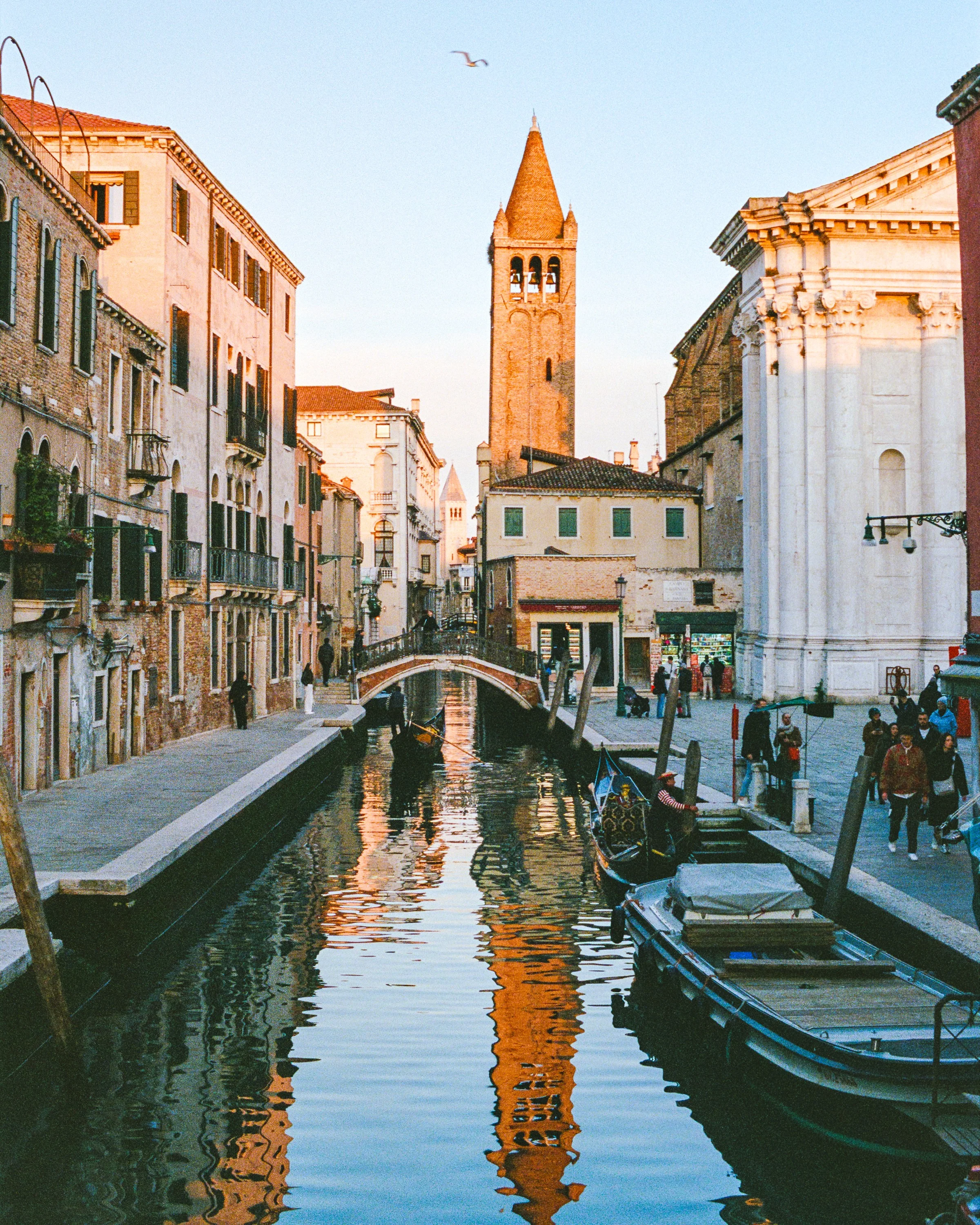 A Venetian canal leading to a brick bell tower, gondolas moored below a white church
