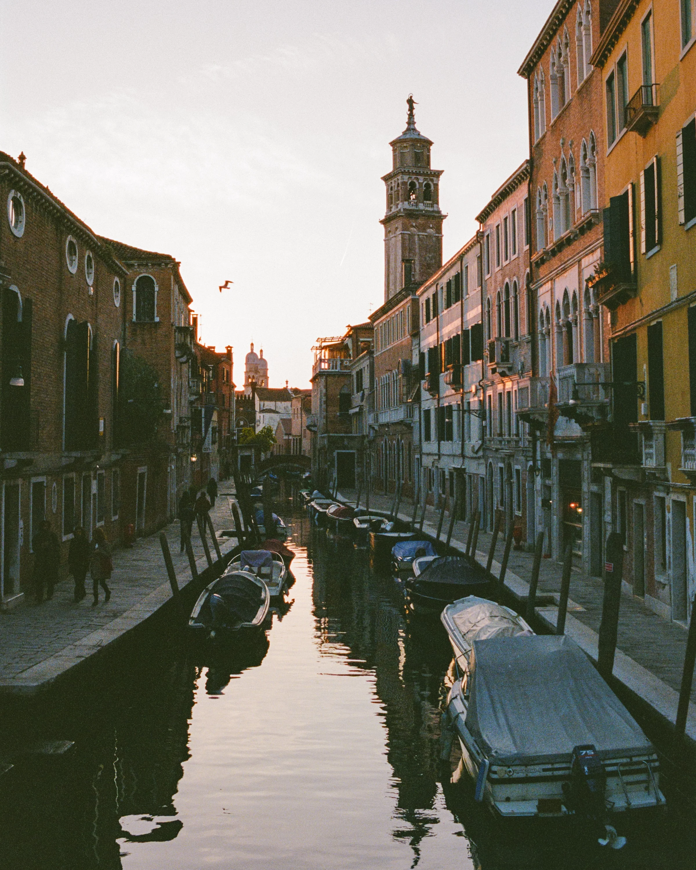 A quiet canal in Venice at dusk, a bell tower at the end