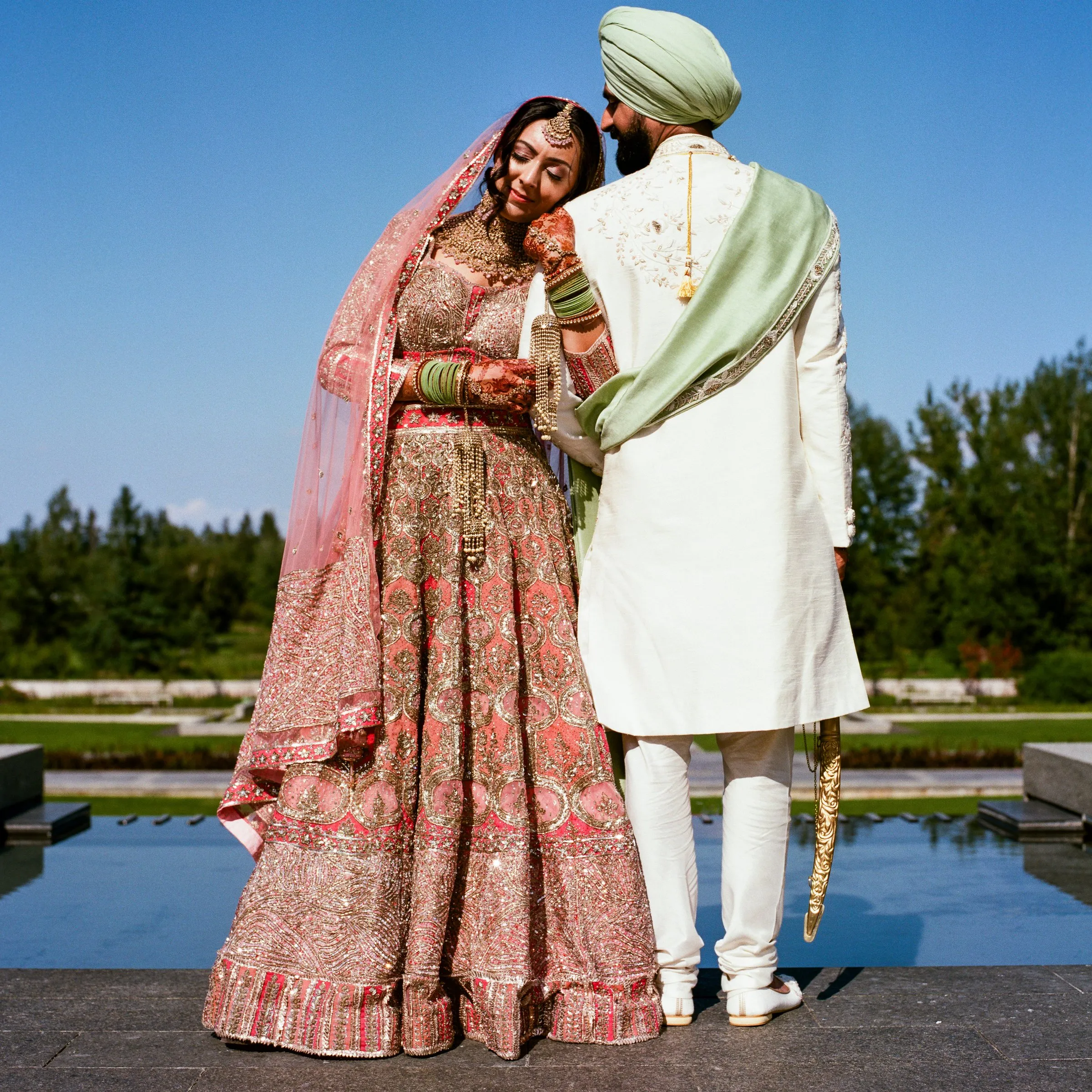 A bride and groom beside a reflecting pool, the bride looking back at the camera