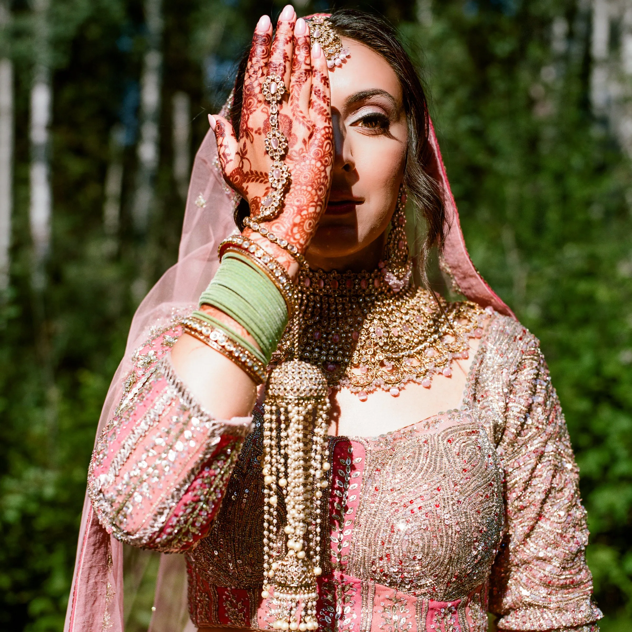 A bride in pink holds a hennaed hand over one eye