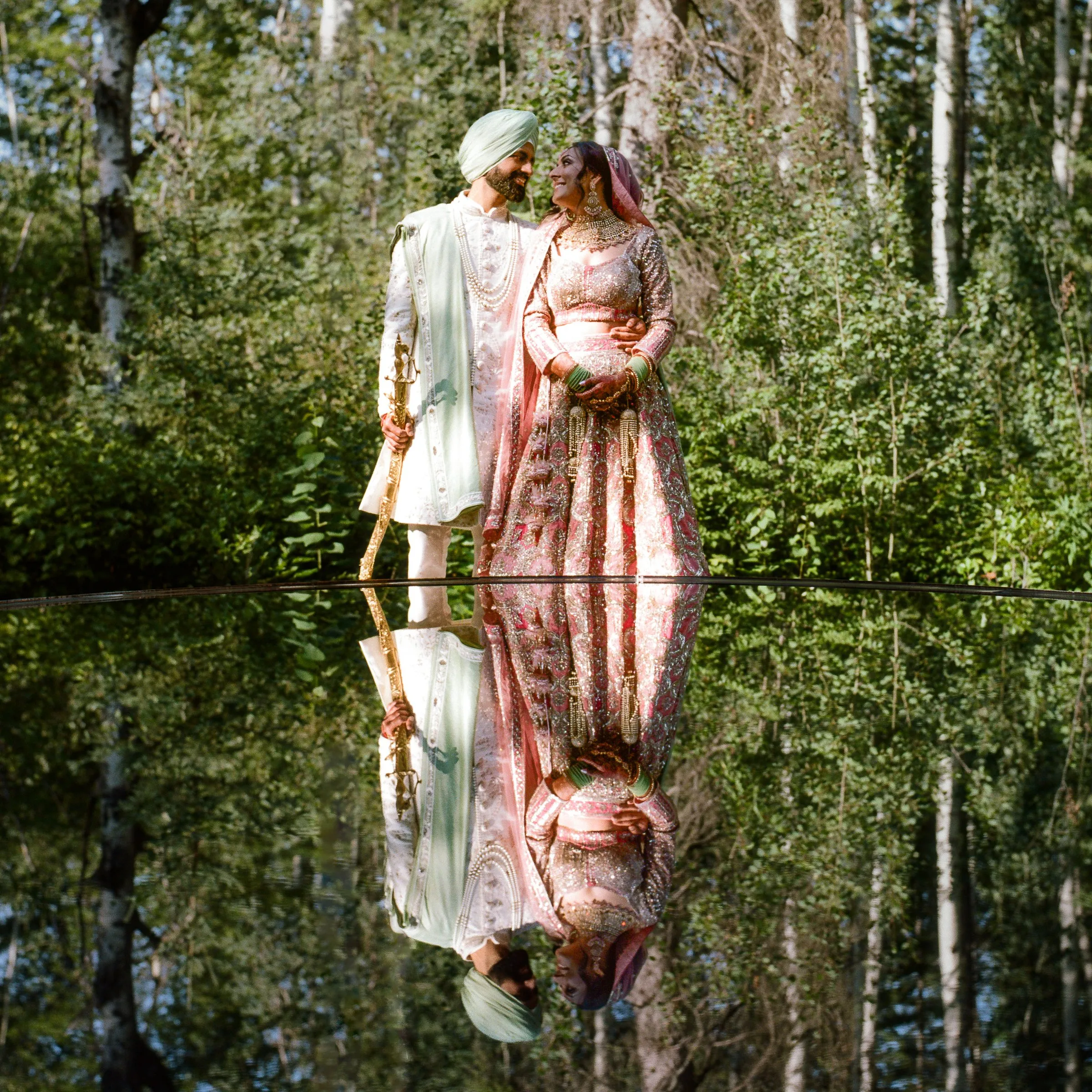 A bride and groom embracing among birch trees, mirrored in still water