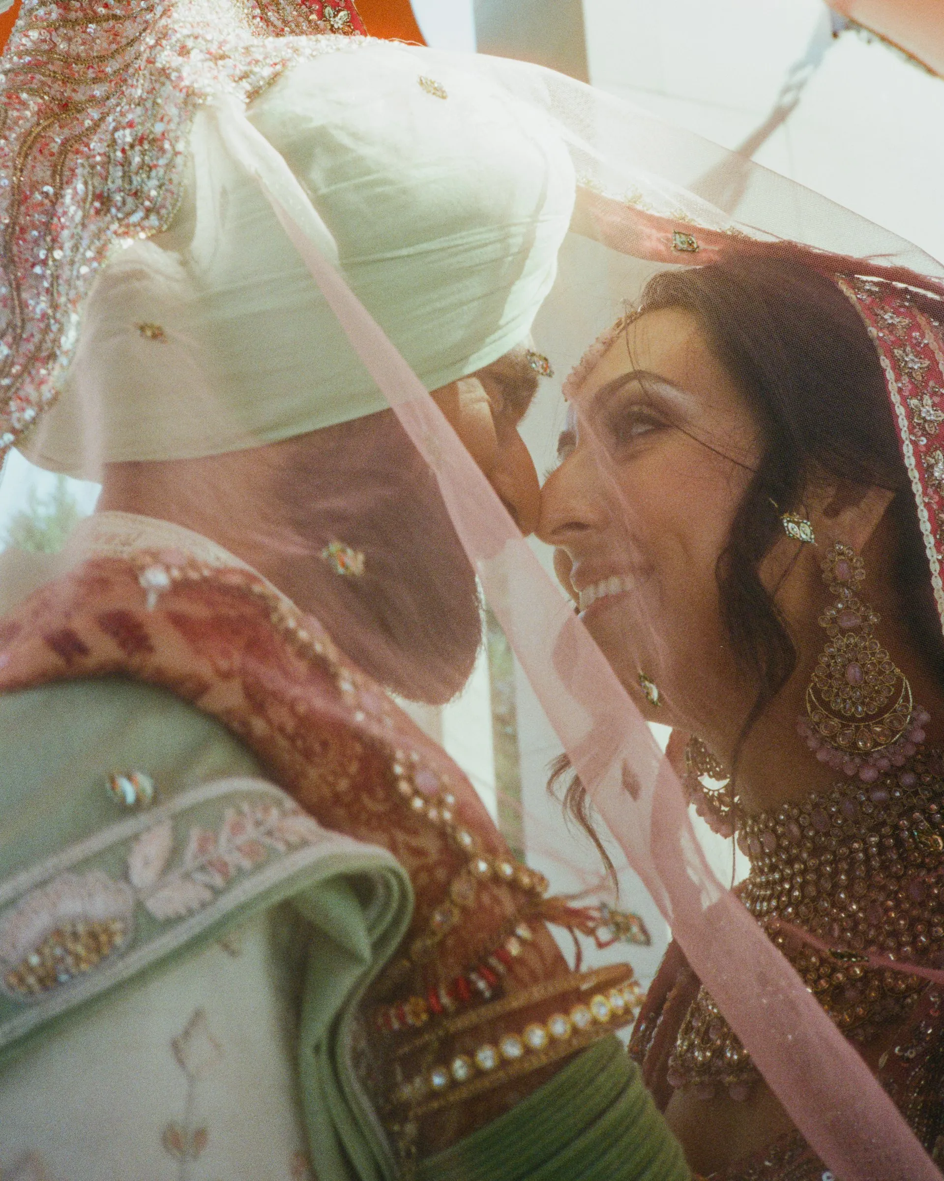 A bride and groom close together under a sheer pink veil