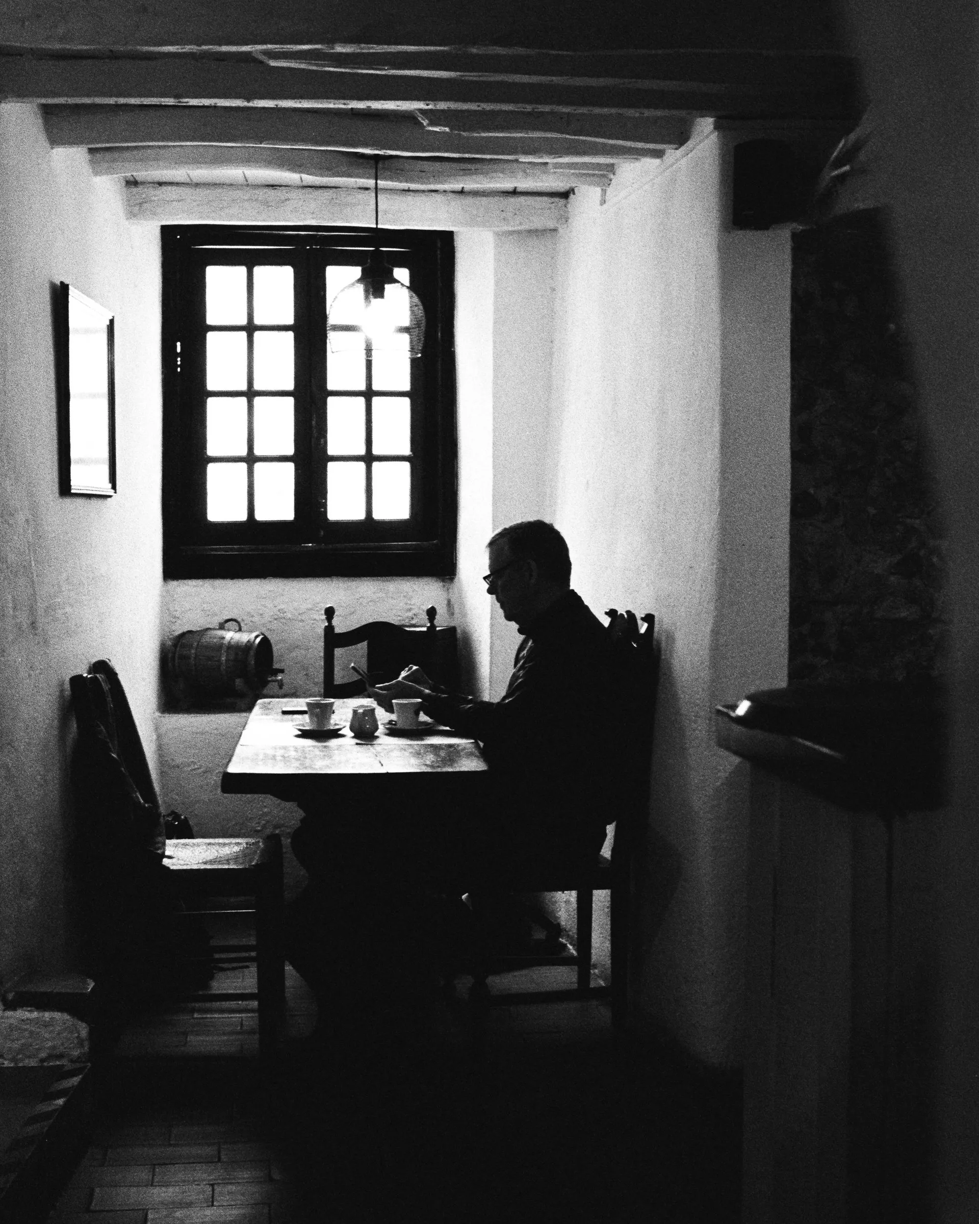 Black and white silhouette of a man sitting at a table by a window