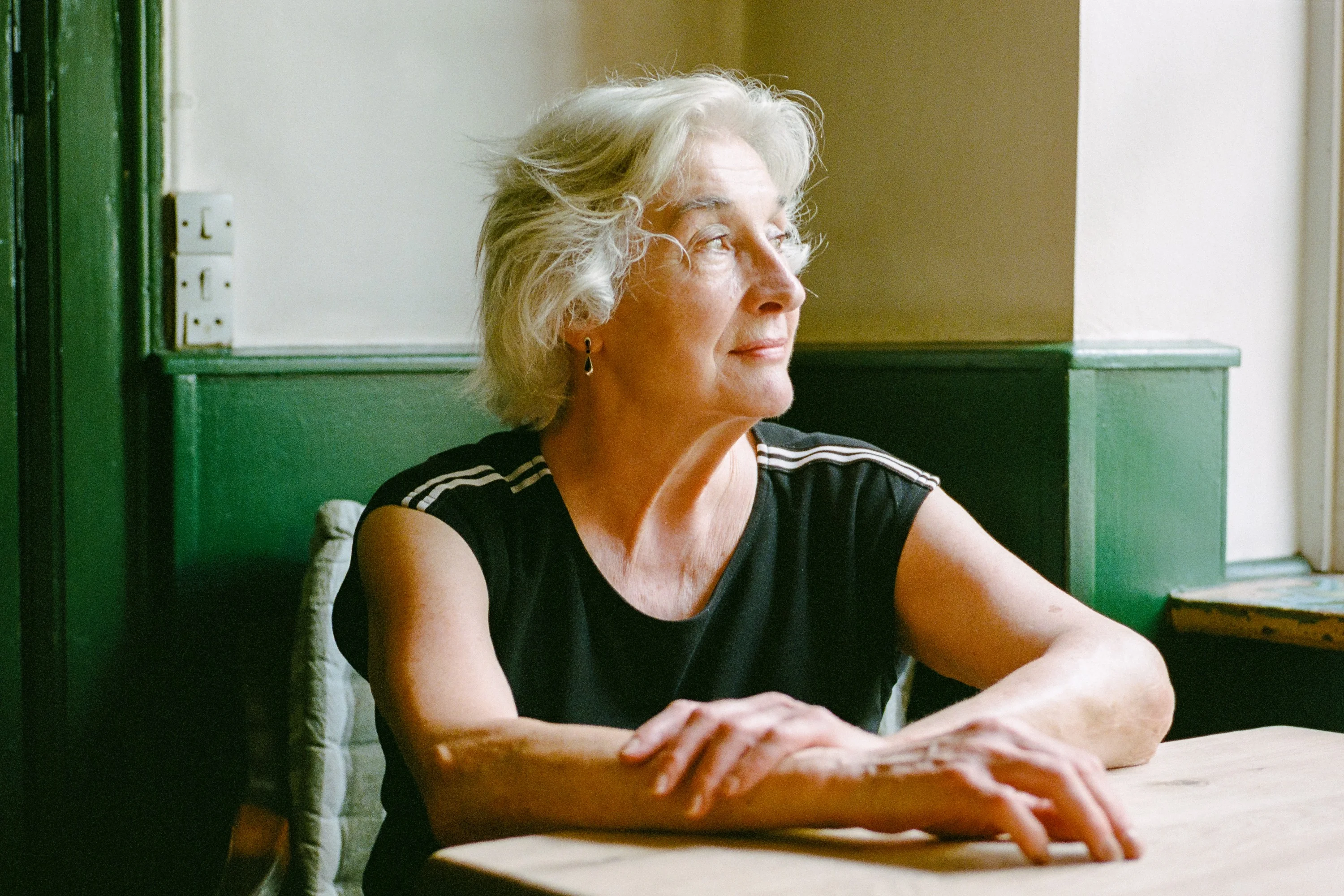 An older woman sitting at a table by a window, looking out