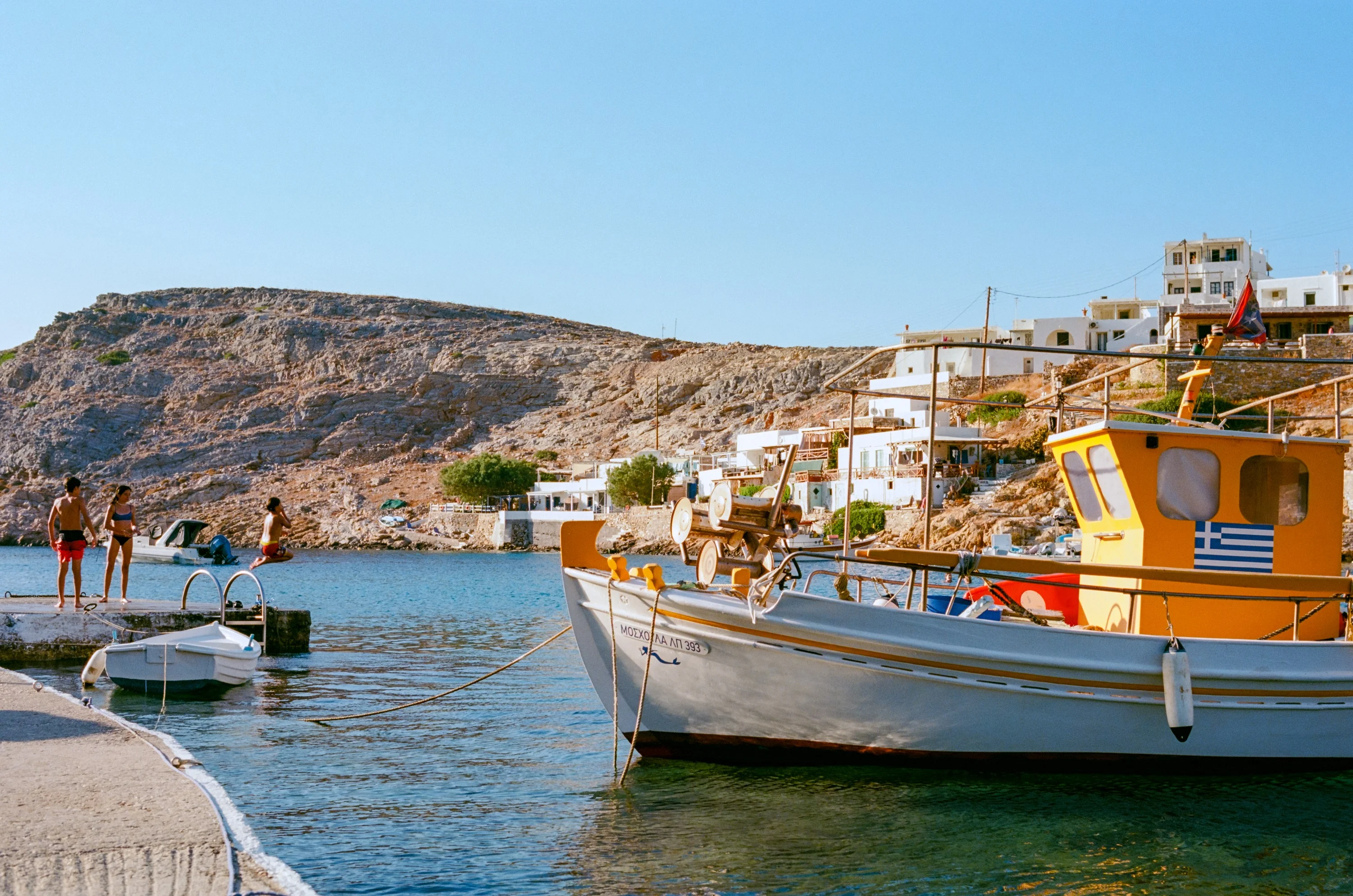 A yellow and white fishing boat moored in a small harbour below a hillside village