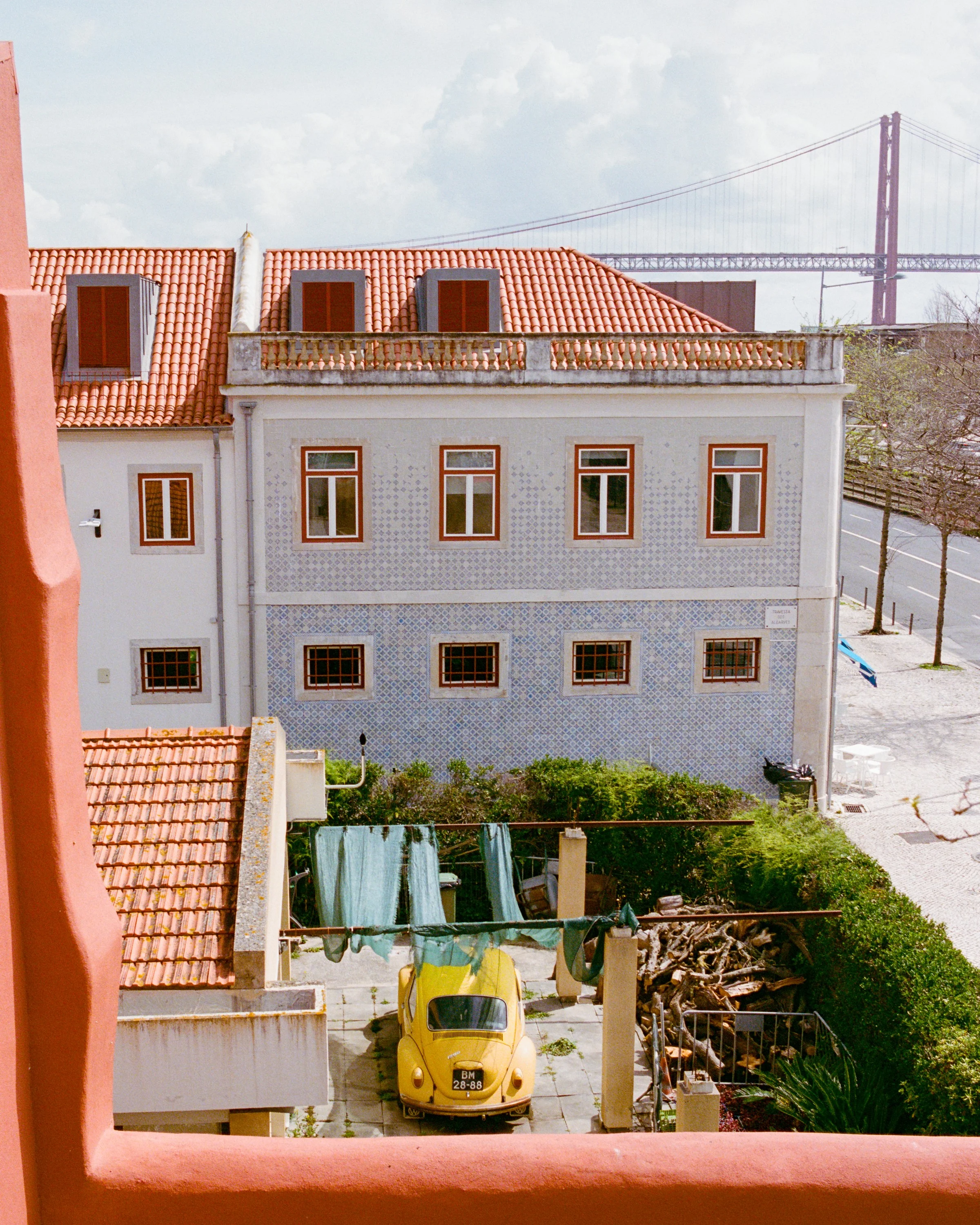 A yellow car in a garden below a tiled house, the bridge behind
