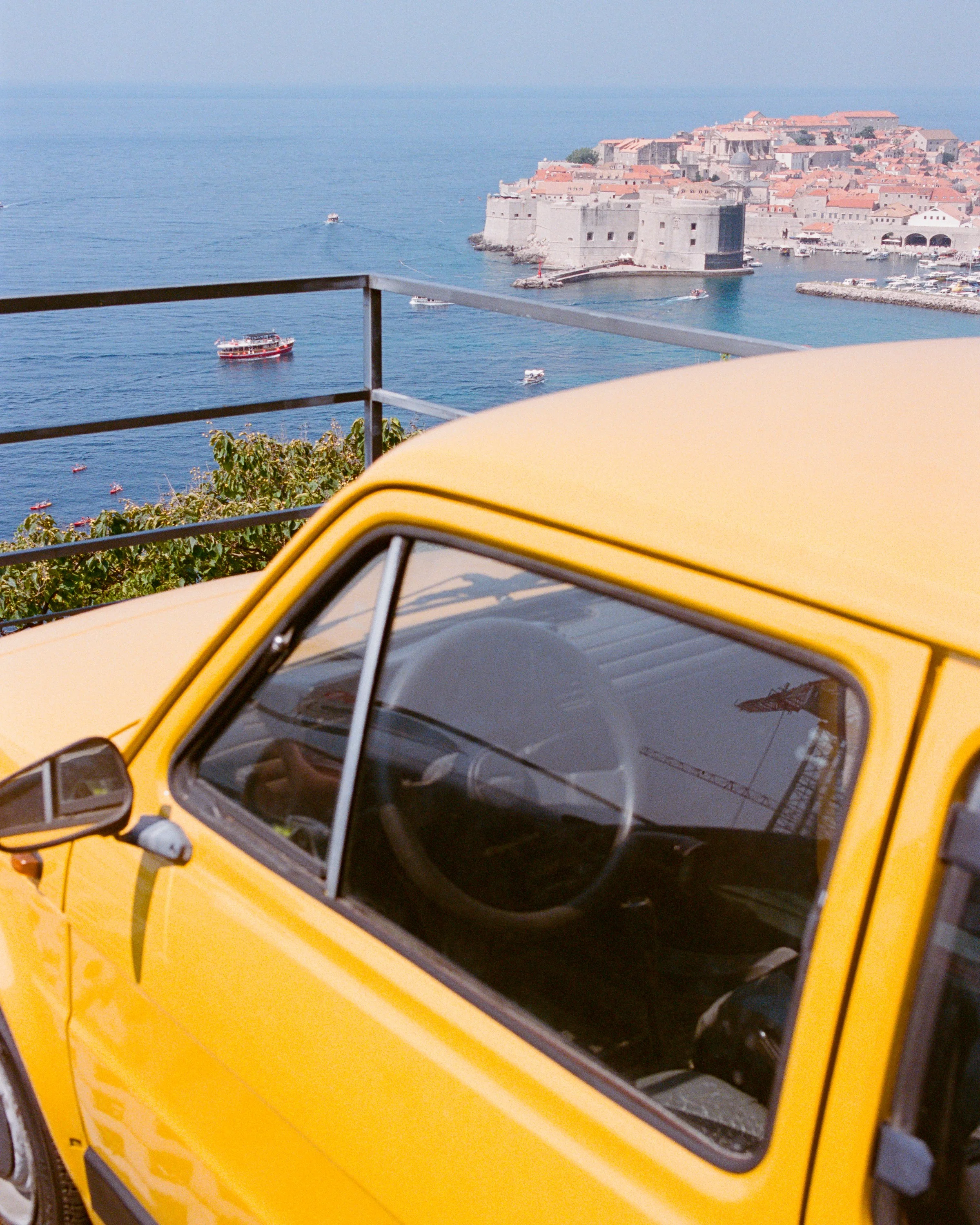 A yellow Fiat 126 parked above the old town and the sea