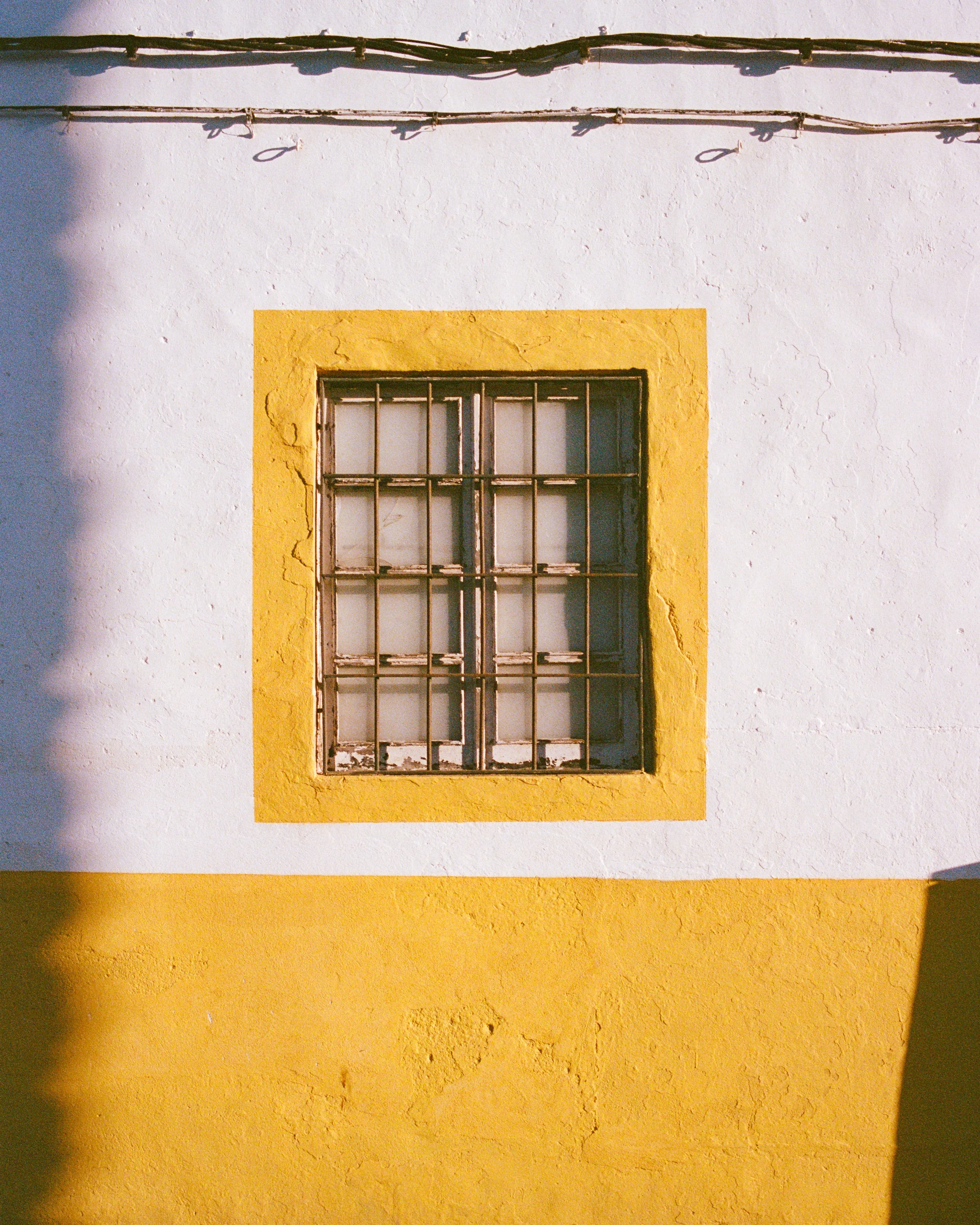 A barred window framed in yellow on a white wall
